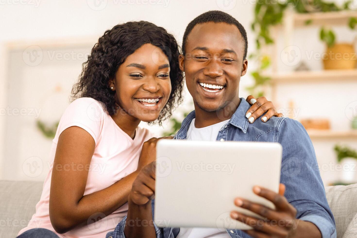Emotional african couple using digital tablet together at home, having call with friends, closeup photo