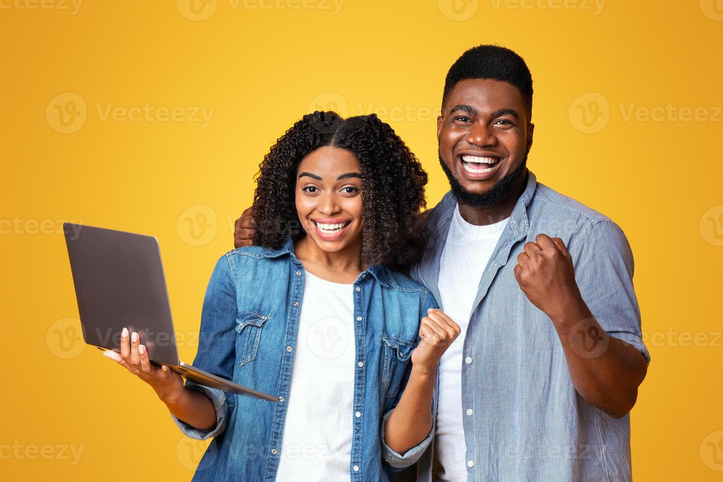 Excited young adults express joy and accomplishment, with one holding a laptop. Their vibrant expressions reflect happiness in a lively, yellow background, suggesting a moment of achievement. photo