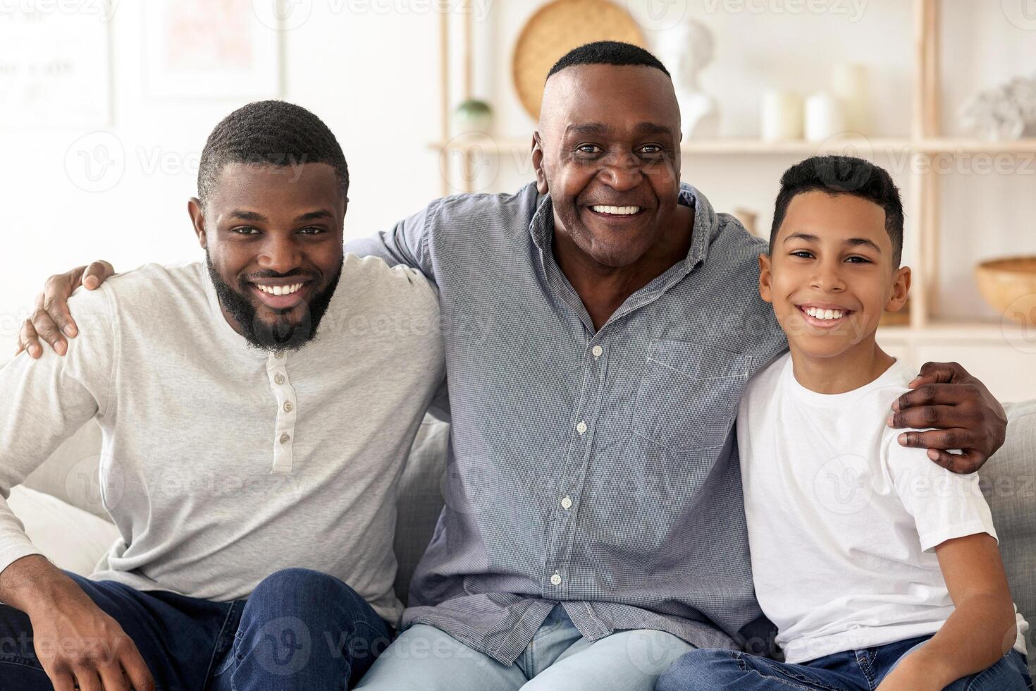 A grandfather, father, and son smile together on a sofa, celebrating family bonds and joy in their cozy living room filled with warm light and modern decor. photo