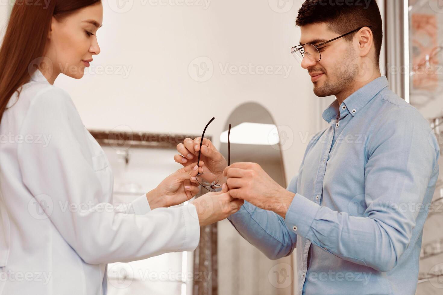 A professional optician helps a man choose a pair of eyeglasses while discussing options. The setting is a modern eyewear shop filled with various frames. photo