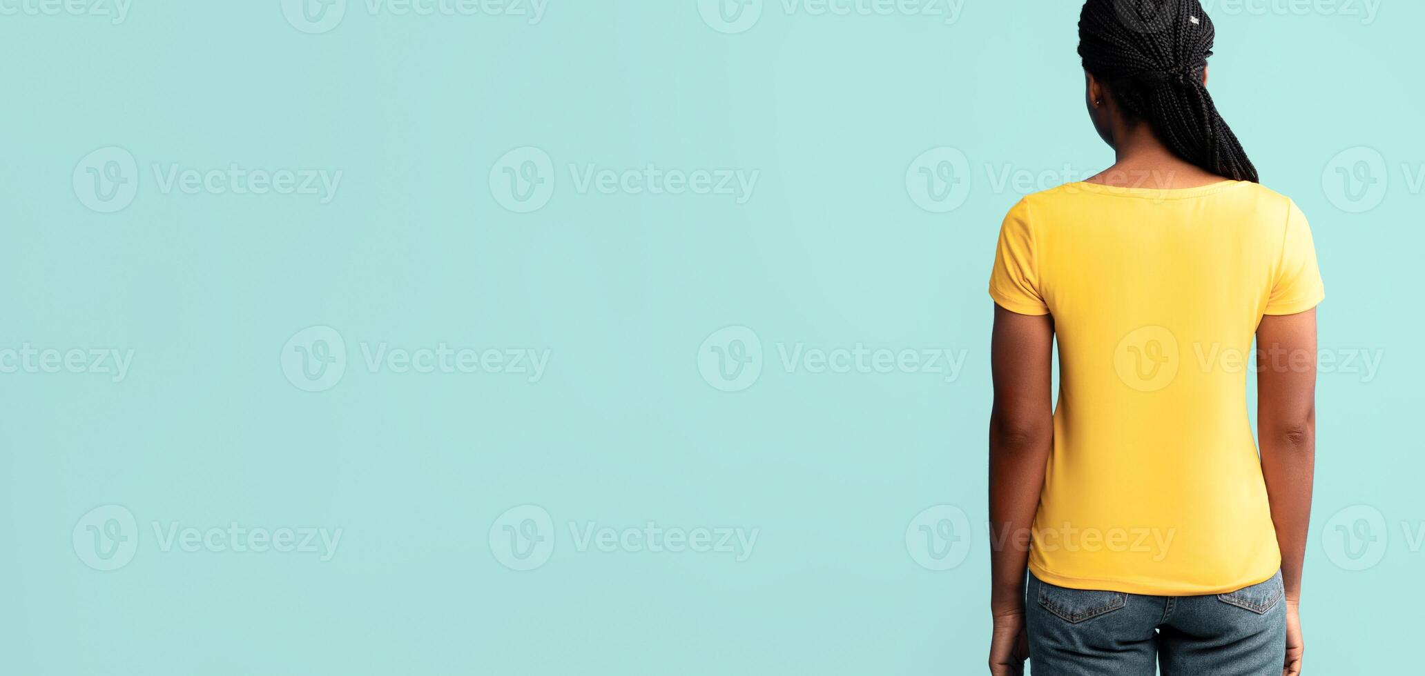 A woman stands with her back to the viewer, wearing a bright yellow shirt. The modern backdrop is a calming teal, creating a vibrant contrast. photo