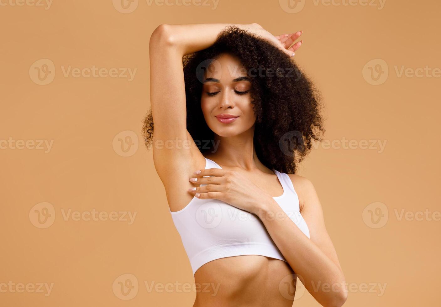 Young black woman with perfect soft armpit skin enjoying results of routine procedures, putting hand up, free space, advertisement for under arm deodorant and epilation, beige background photo