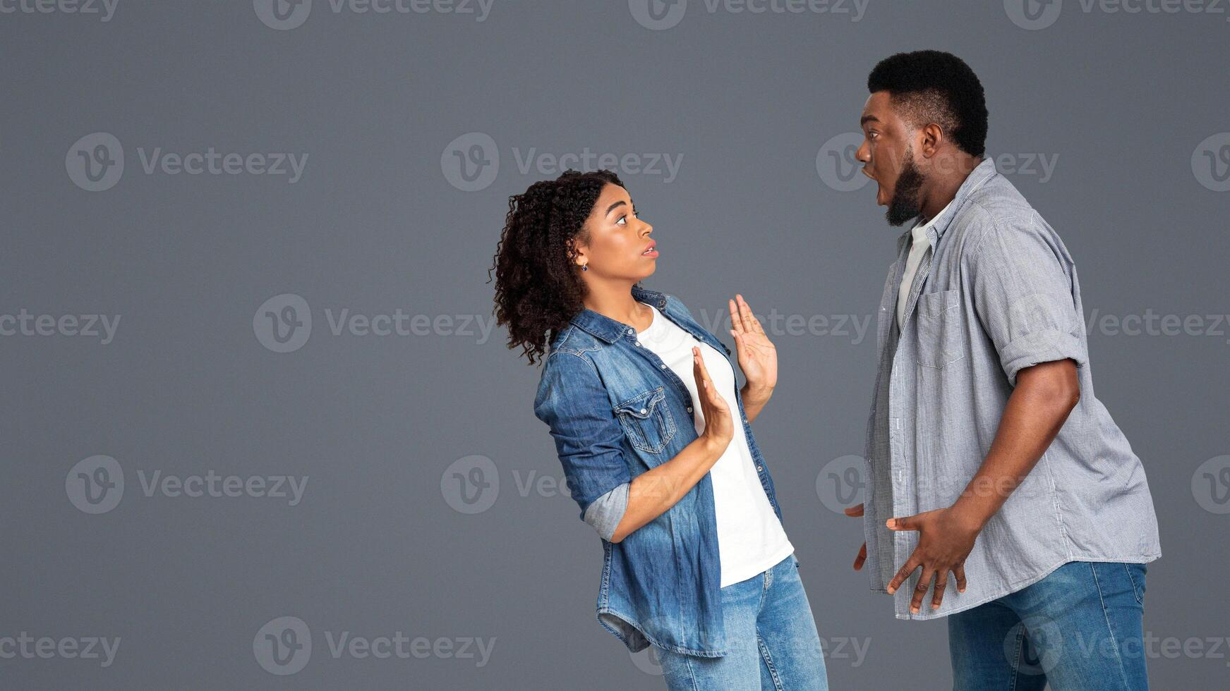 A woman standing with her hands raised appears surprised while a man facing her expresses enthusiasm or excitement. They engage in a lively conversation in a simple indoor setting. photo