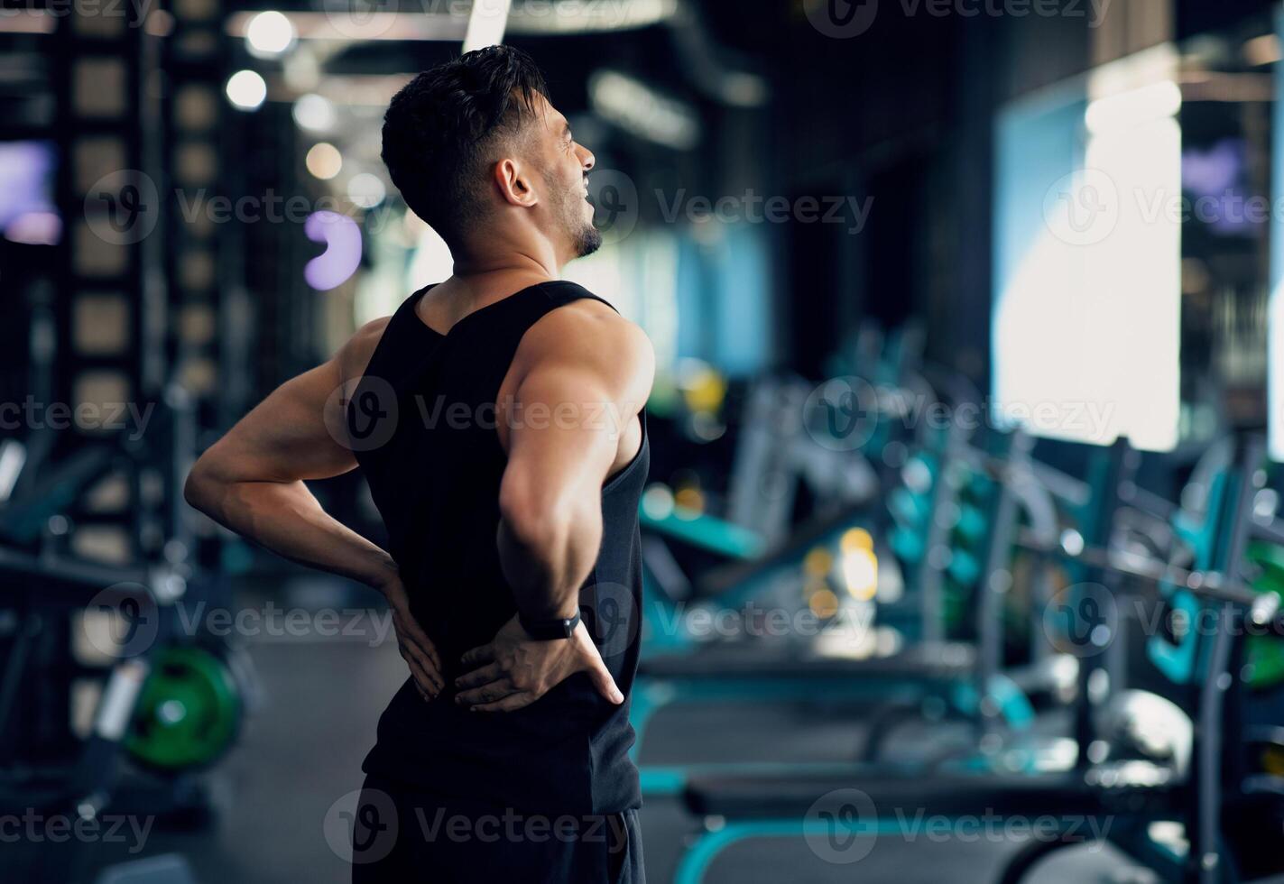 Portrait Of Young Arab Bodybuilder Suffering Lower Back Pain At Gym, Upset Middle Eastern Male Athlete Rubbing Painful Sore Zone After Getting Sport Injury, Having Lumbar Spine Ache, Copy Space photo