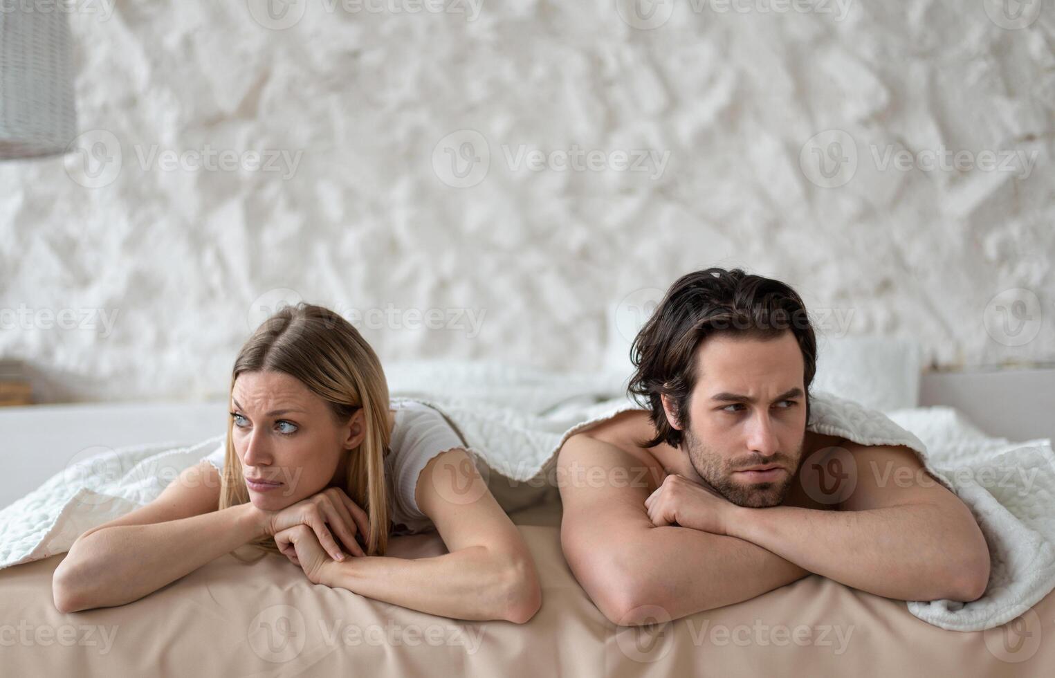 Sexual problems, relationship crisis. Stressed young couple lying in bed, overwhelmed with family difficulties, not speaking after conflict, suffering from erectile dysfunction or lack of libido photo