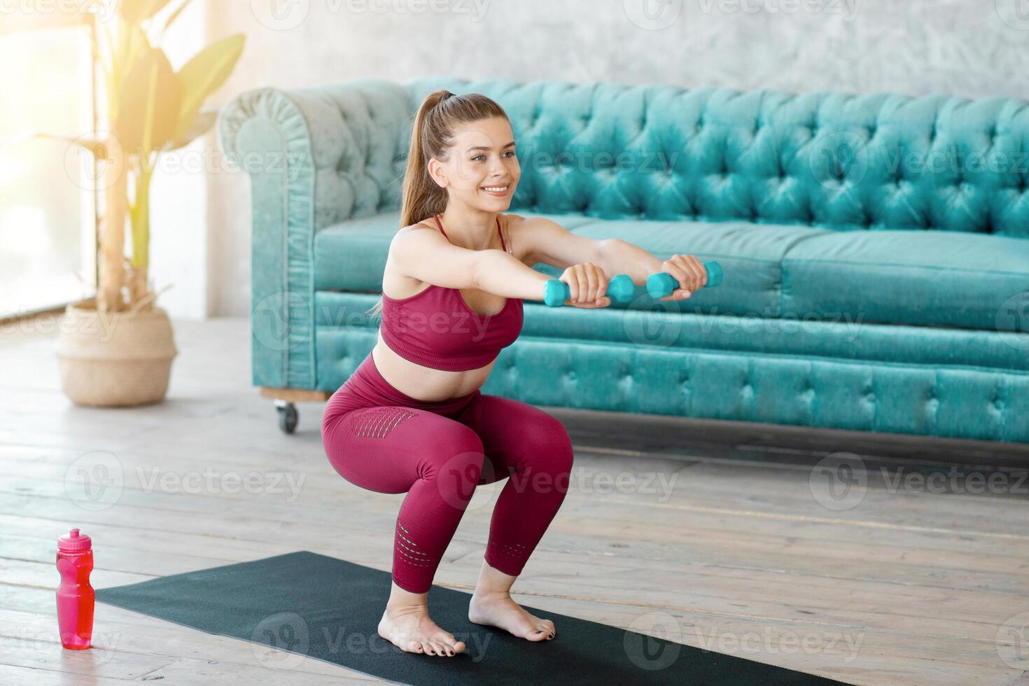 Strength workout at home. Lovely woman with dumbbells doing squat exercise in living room photo