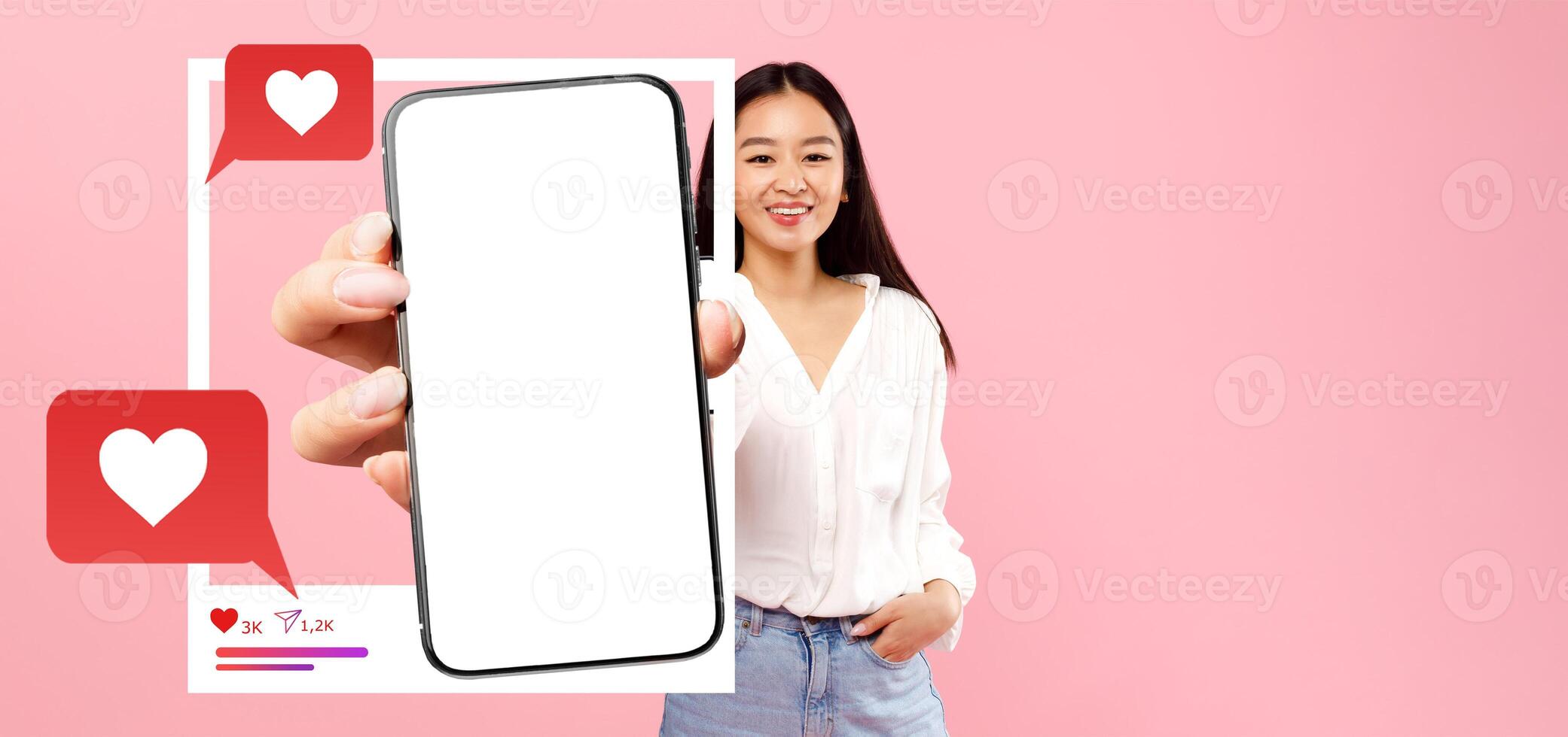 An influencer smiles while holding a blank smartphone in front of a pink background, highlighting social media engagement elements like hearts and chat bubbles, perfect for online content promotion. photo