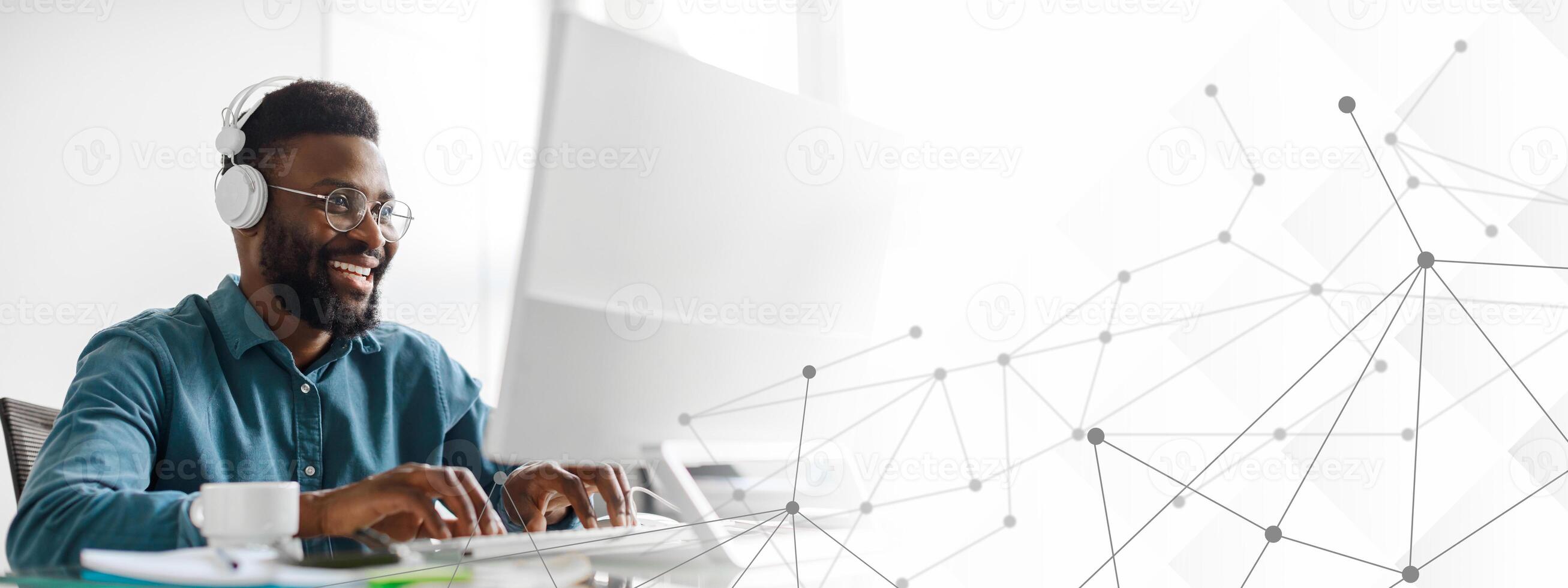 A young African American entrepreneur is focused on his work while wearing headphones in a contemporary office setting. He engages with technology, embodying success and a modern lifestyle. photo