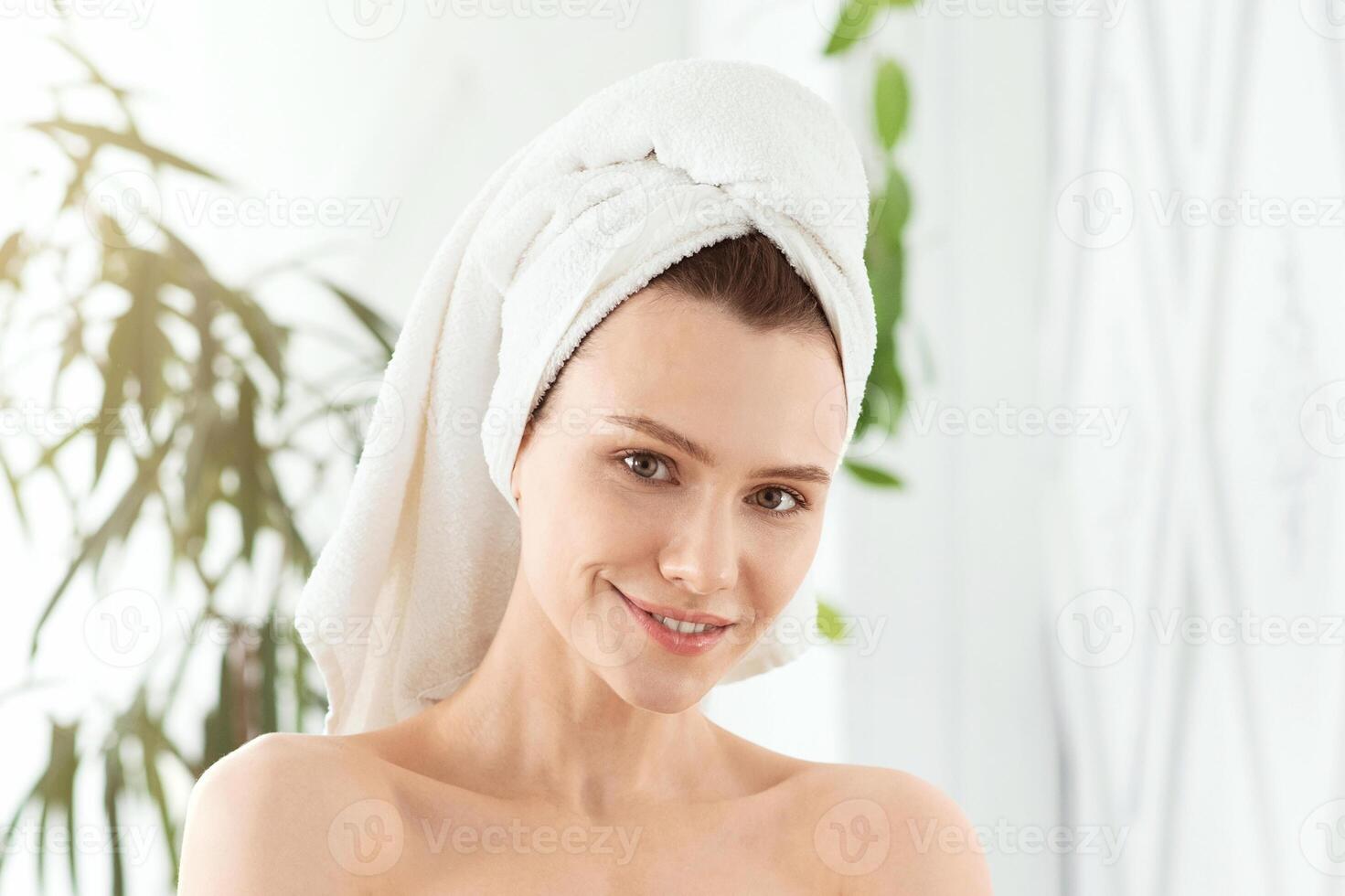 Prertty young woman wrapped in towels after morning shower posing in bedroom at home, copy space. Attractive smiling lady embracing herself, touching her smooth young skin, body care concept photo
