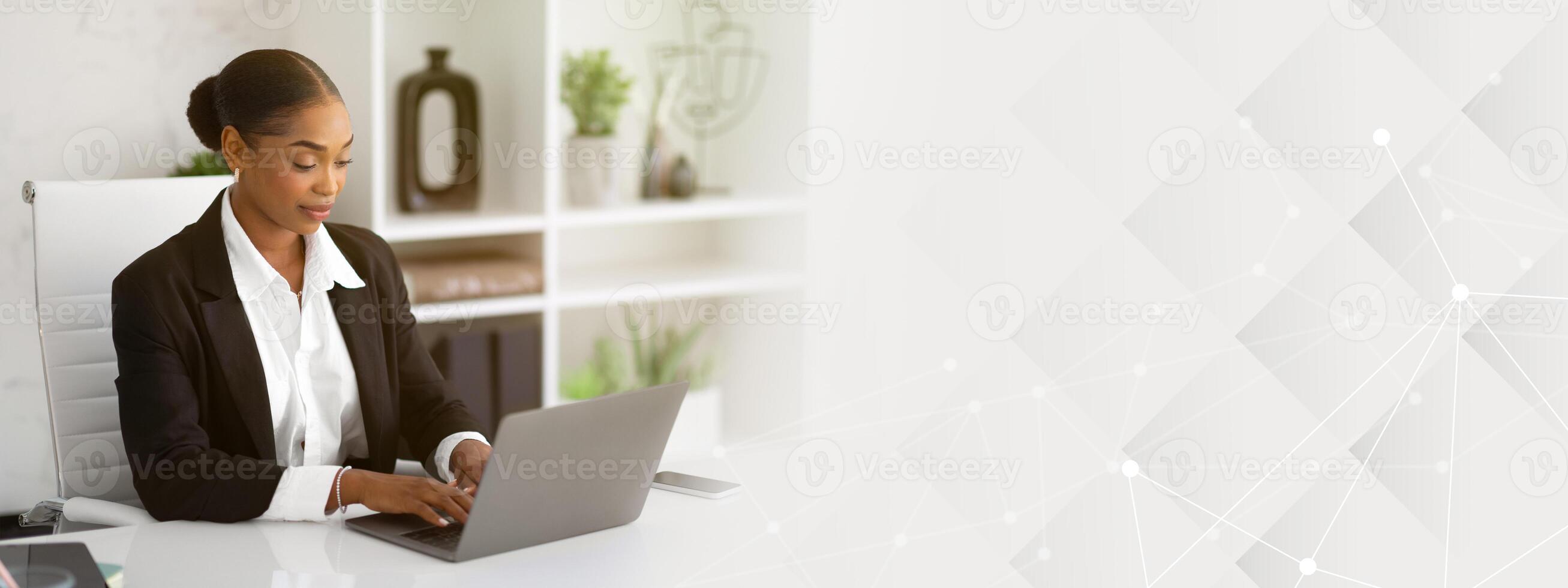 Beautiful black businesswoman in formal wear working with laptop computer at desk in office interior, typing document, checking email, participating in online meeting at workplace photo