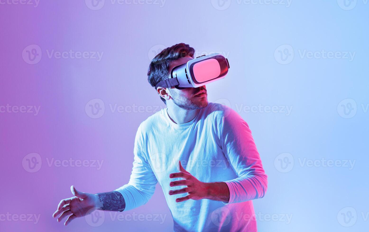 A man is fully immersed in a virtual reality experience, wearing a VR headset. He displays a surprised expression as he interacts with an unseen digital environment. photo