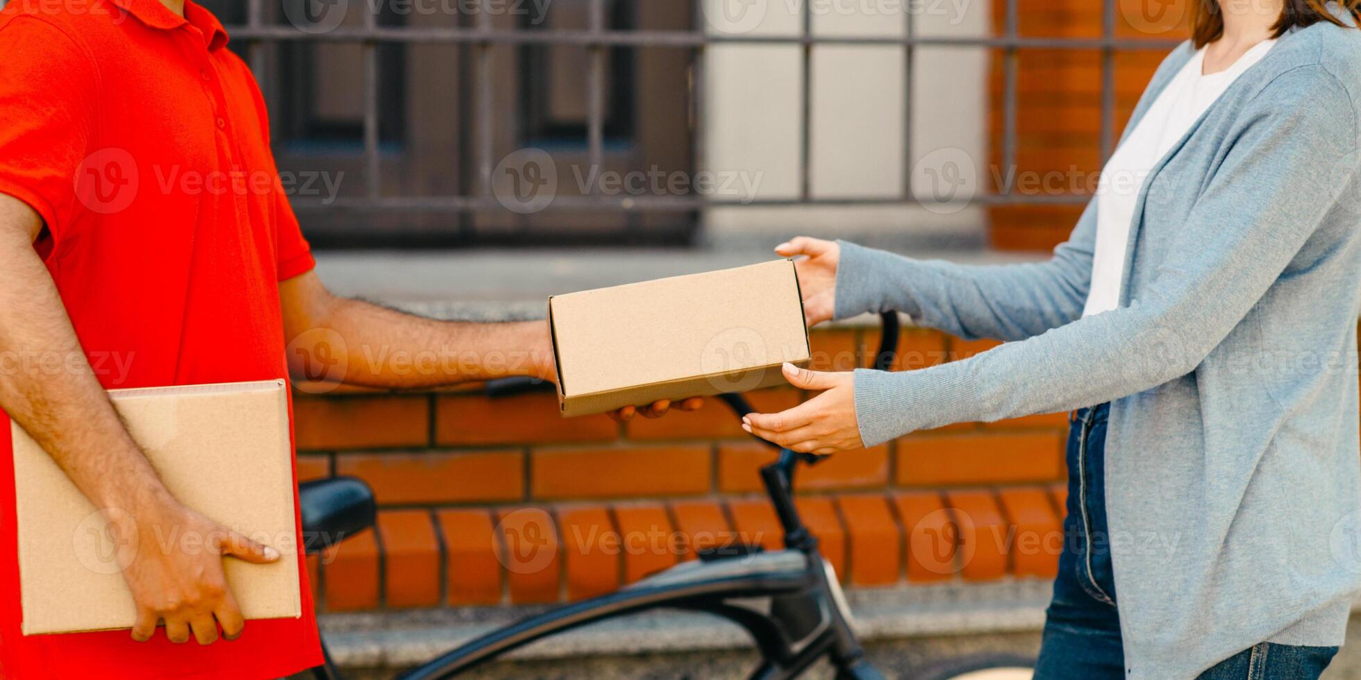 Online ordering. Client received package from bicikle courier in uniform, near front door on street, cropped, panorama, copy space photo