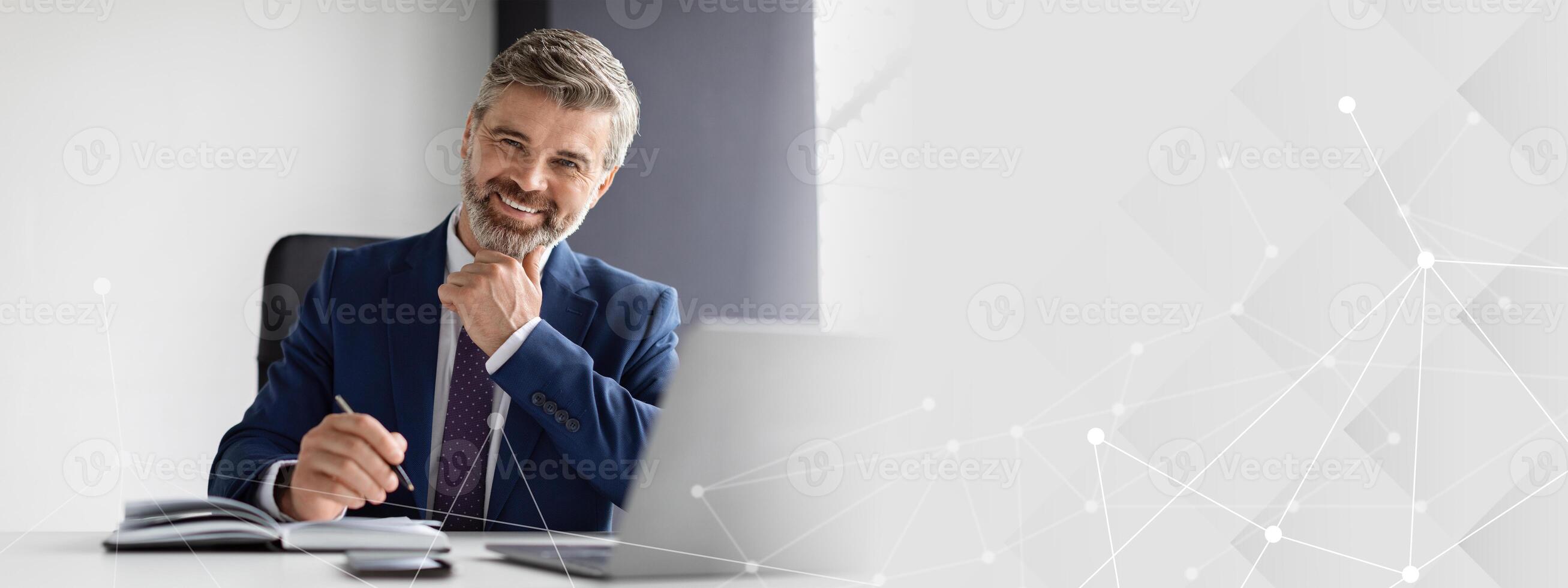 Portrait Of Successful Mature Businessman Wearing Suit Sitting At Desk With Laptop In Modern Office, Smiling Middle Aged Man Entrepreneur Posing At Workplace And Looking At Camera, Copy Space photo