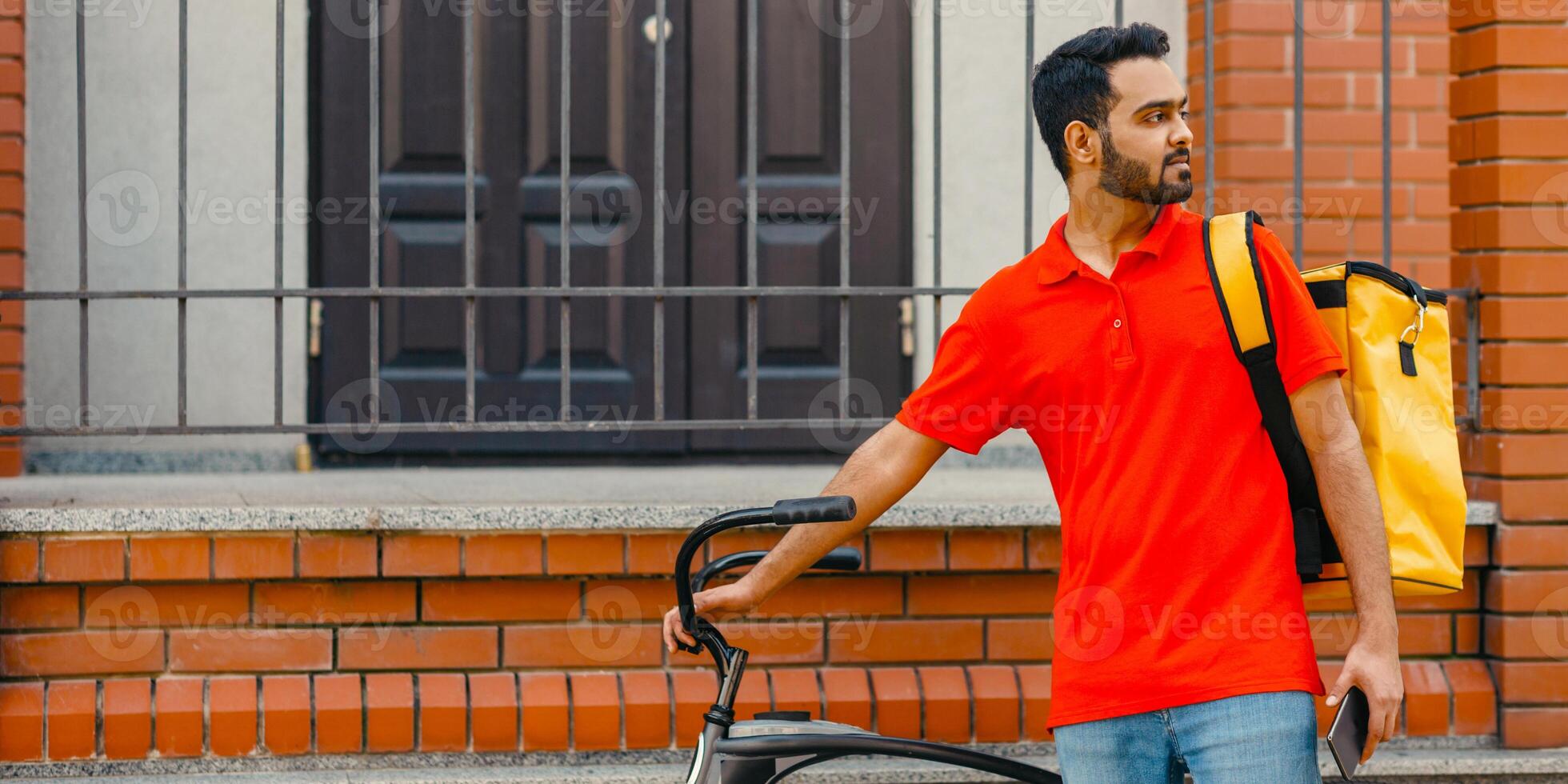 Courier with bicycle, delivery food service at home. Man with beard with mobile phone finds address in city, free space photo