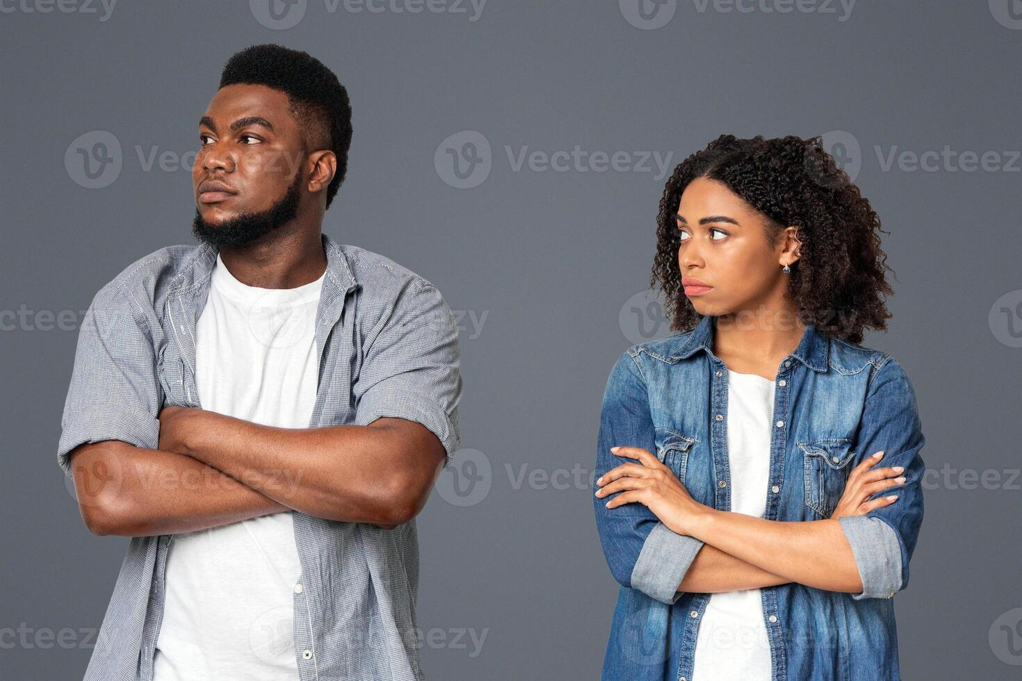 A man and woman stand facing away from each other with crossed arms, expressing clear tension or disagreement. They appear uncomfortable, highlighting a moment of conflict. photo