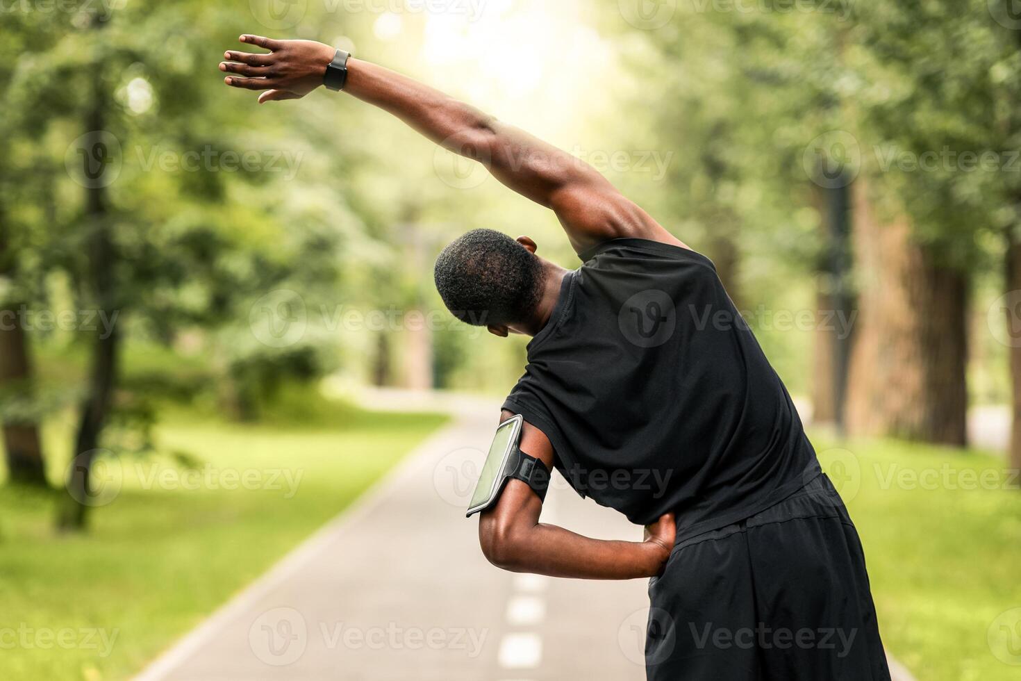 Black sportsman exercising before jogging at park, back view, copy space photo