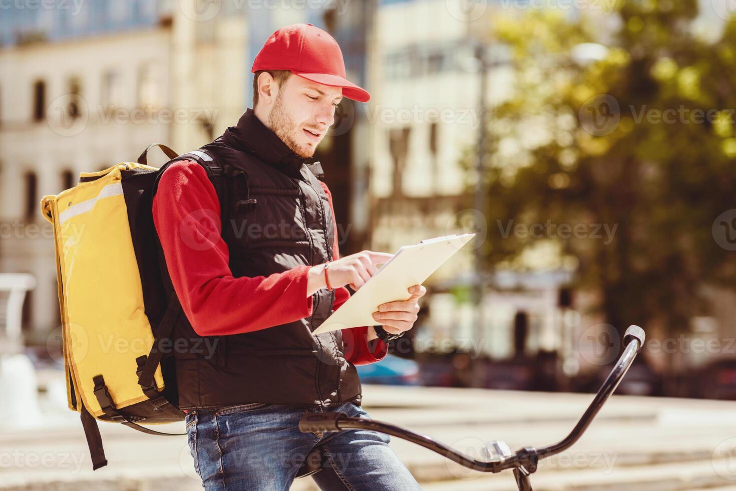 Meal Delivery Service. Courier Delivering Food From Restaurants Checking Orders Holding Folder Standing With Bicycle In City photo