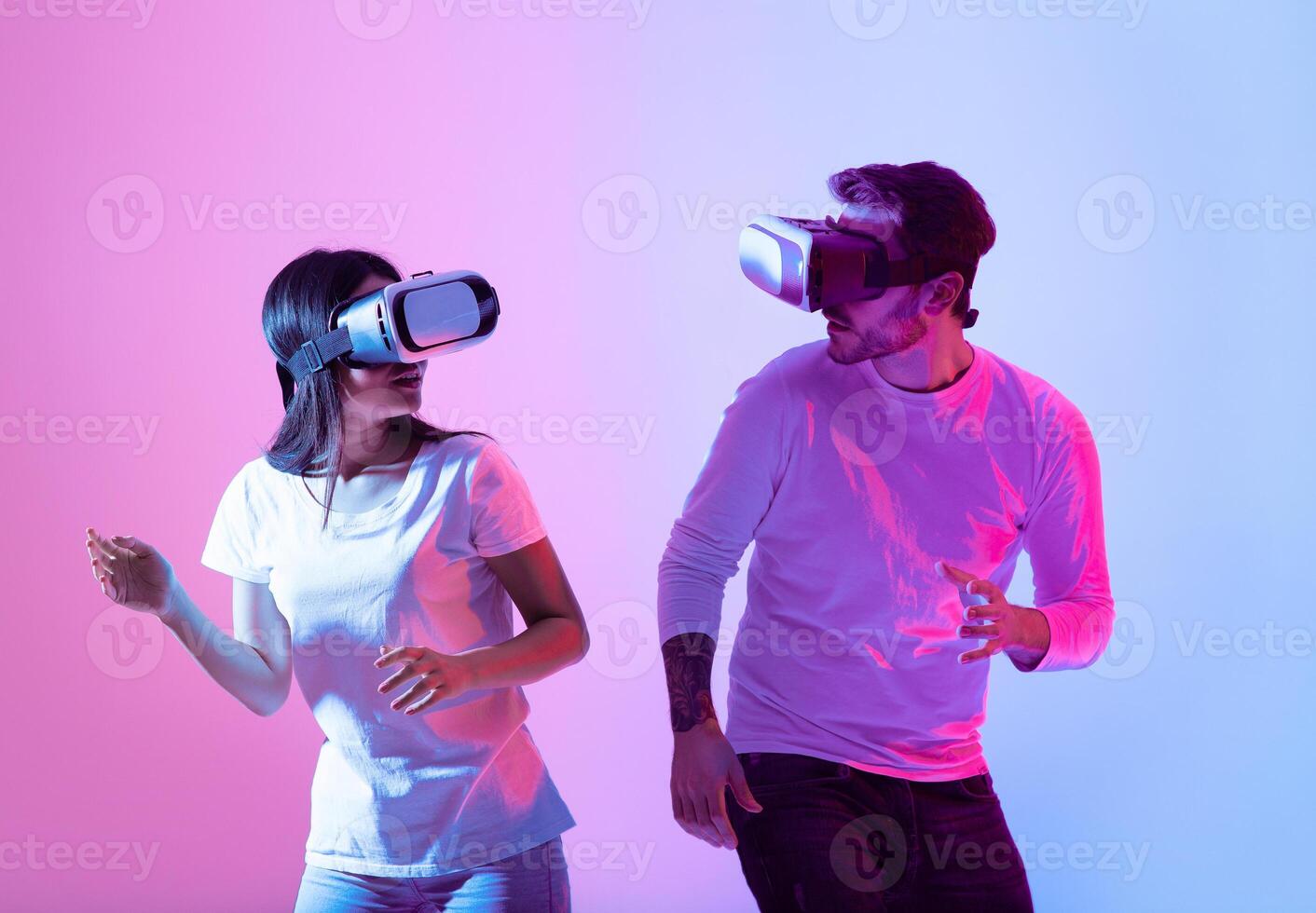 Two individuals engage in a virtual reality activity, wearing headsets and laughing as they navigate an immersive digital world, illuminated by colorful lighting. photo