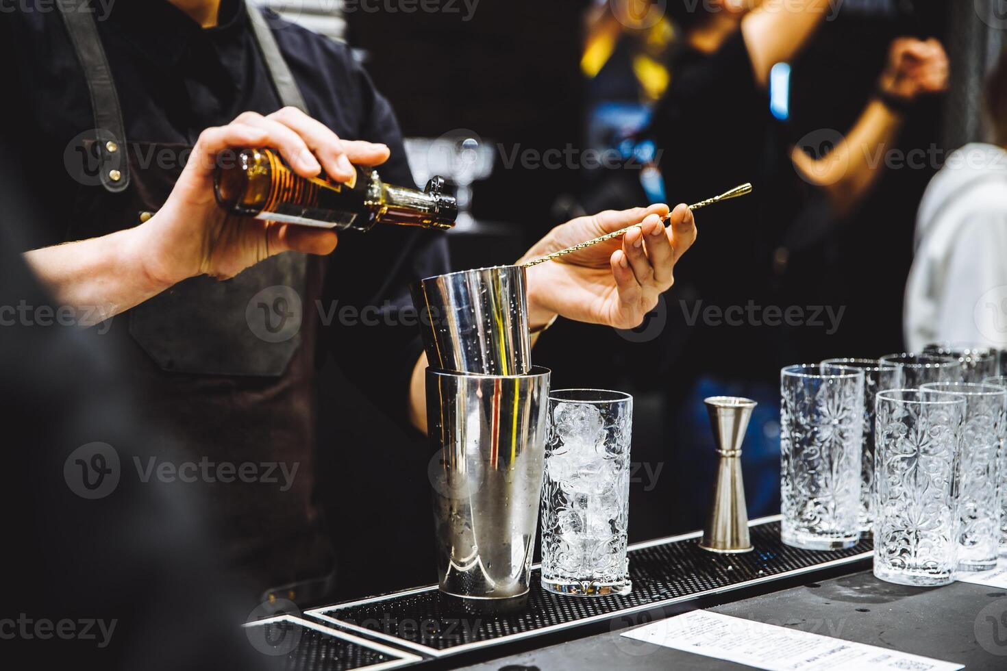 Barman at work pouring hard spirit into glasses and preparing cocktails in detail photo