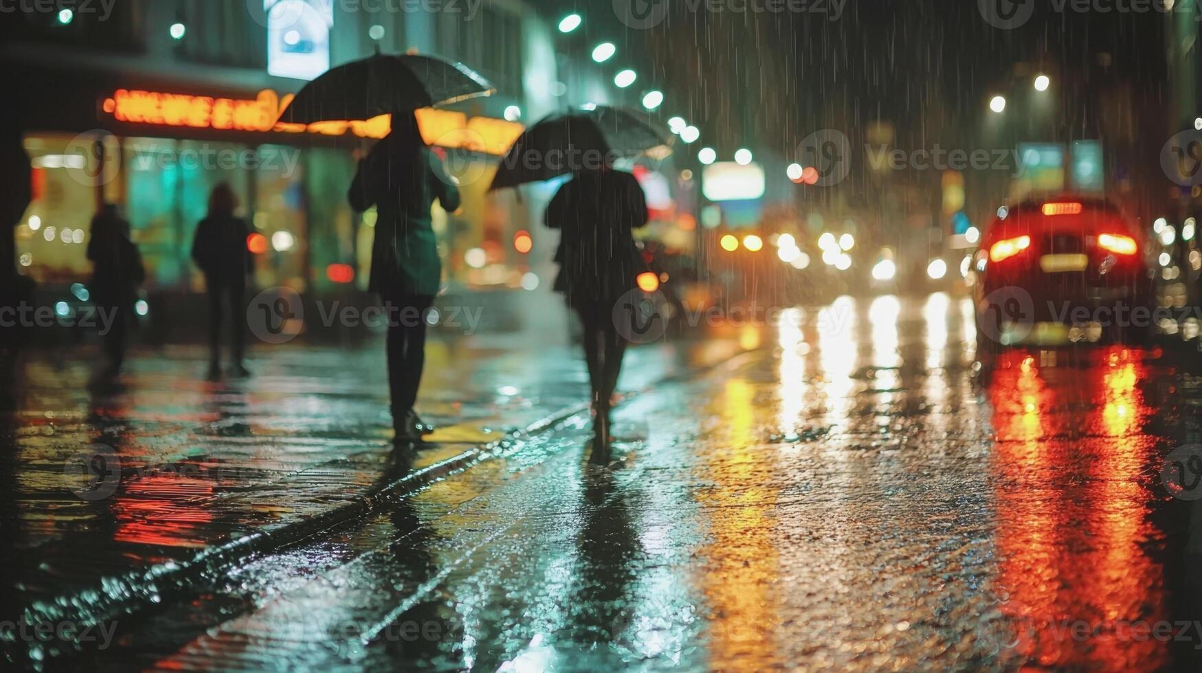 Two individuals walk under umbrellas along a vibrant city street illuminated by colorful lights reflecting off wet pavement during a nighttime rain photo