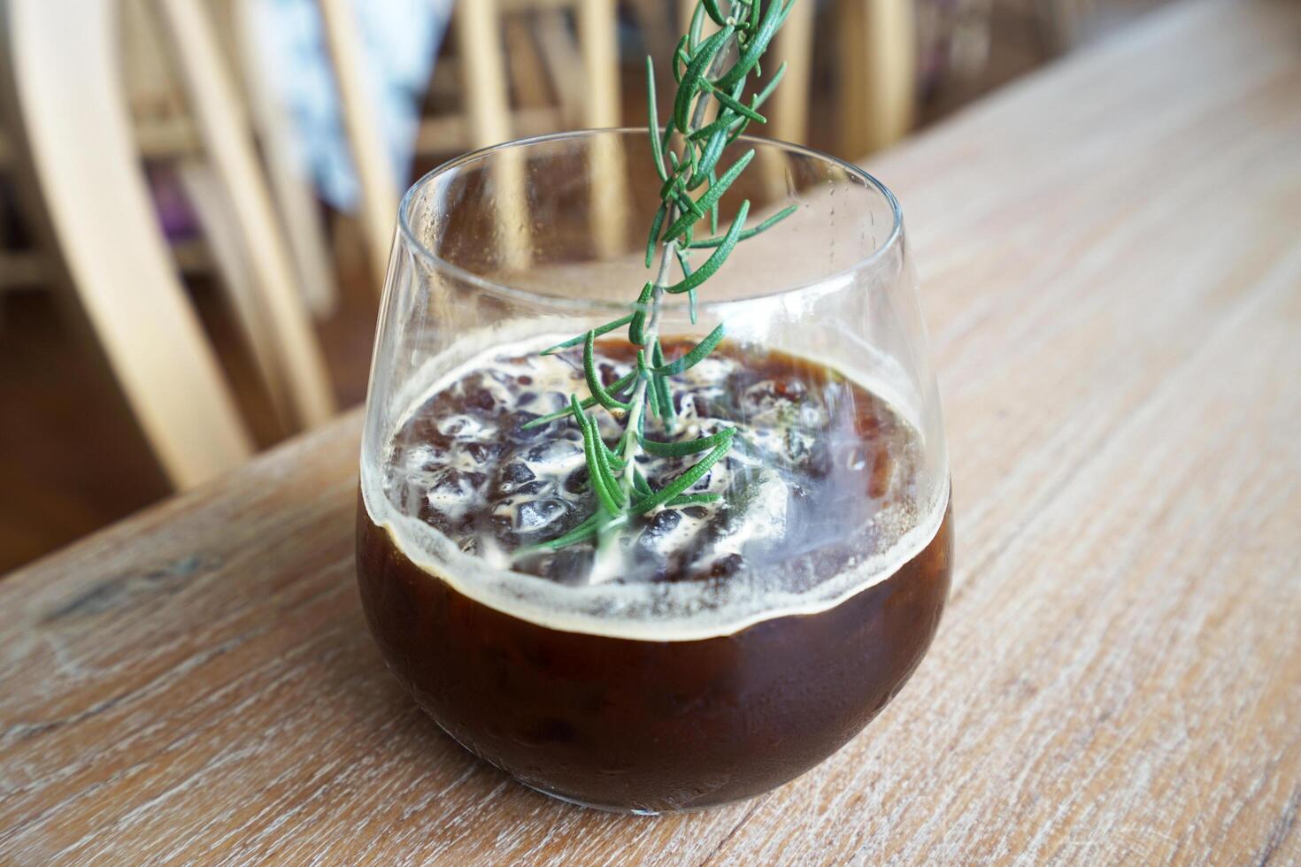 Close up glass of iced black Americano coffee with rosemary on wooden table photo
