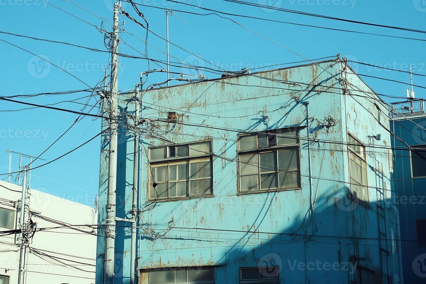 A weathered blue building with power lines against a clear sky. photo