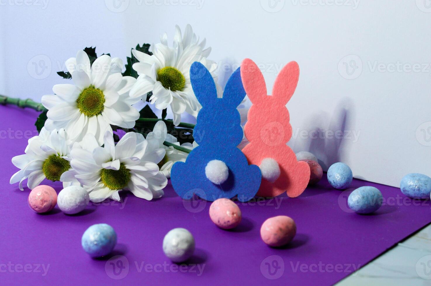 Easter decoration with eggs, rabbits and daisies on a purple background photo