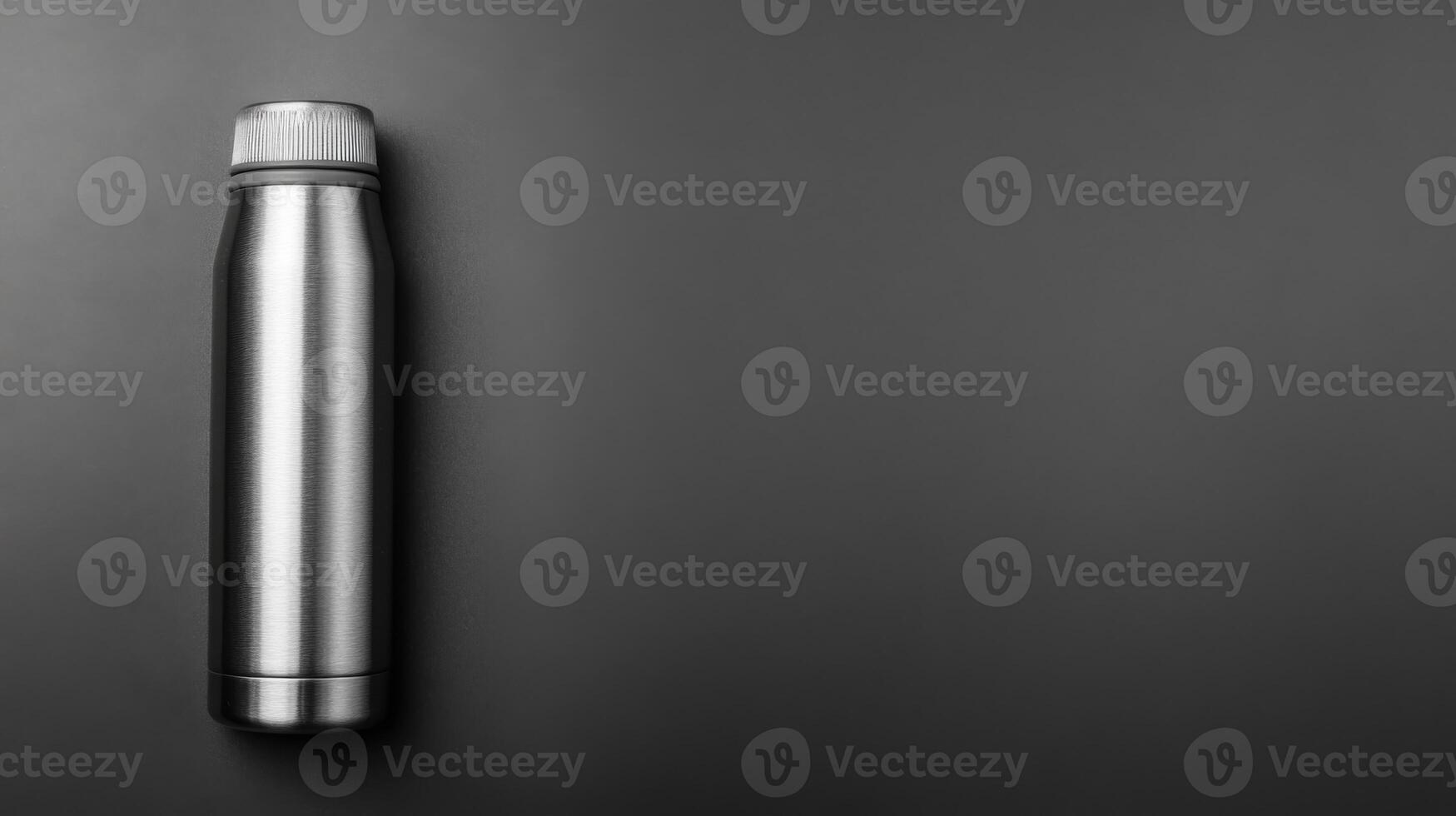 Stainless steel thermos flask on dark backdrop photo