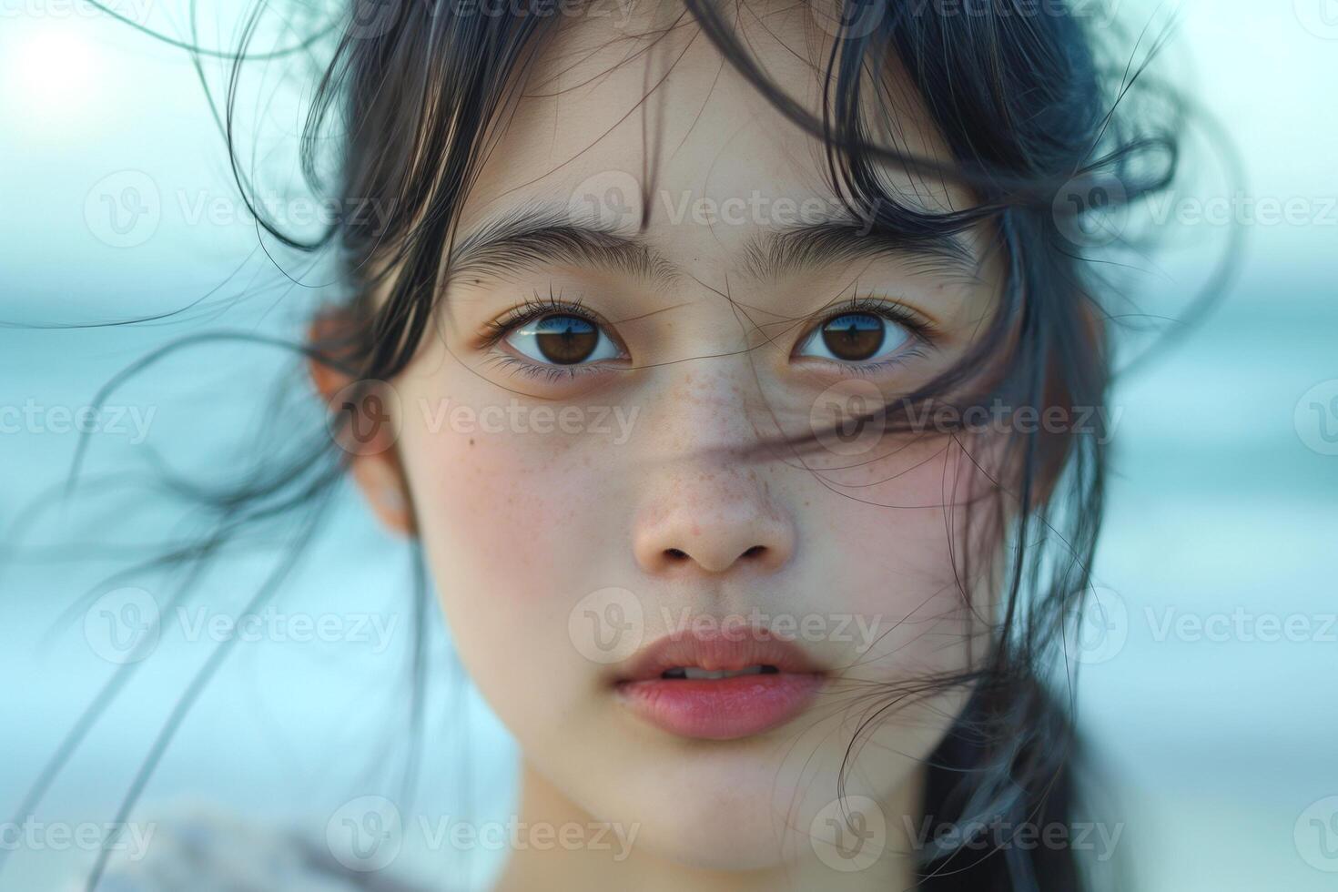 Close-up of a young Asian girl with flowing hair by the beach, conveying a serene and dreamy expression. photo