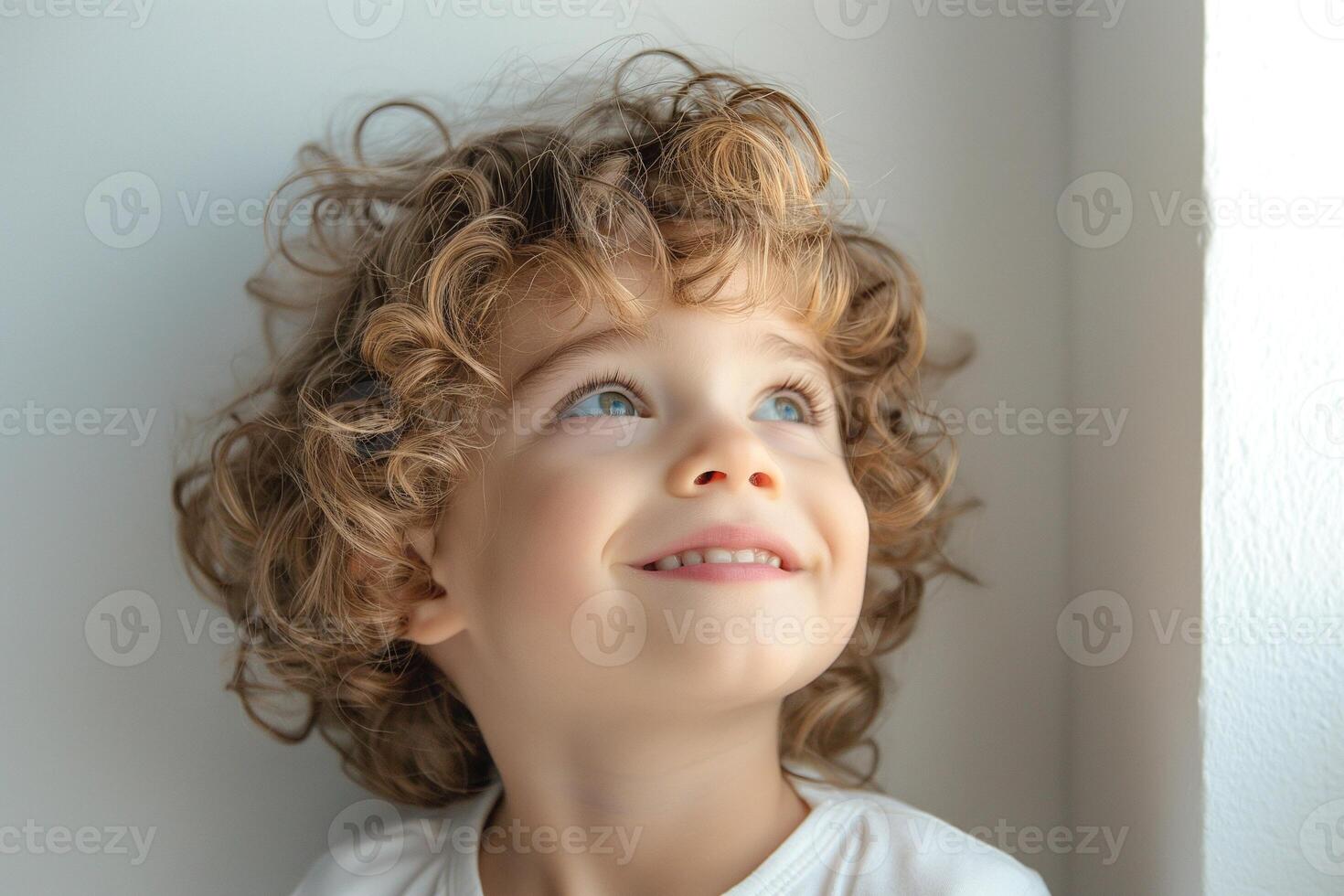 A cheerful Caucasian boy with curly hair gazes upwards, illuminated by soft natural light, showcasing his joyful expression. photo