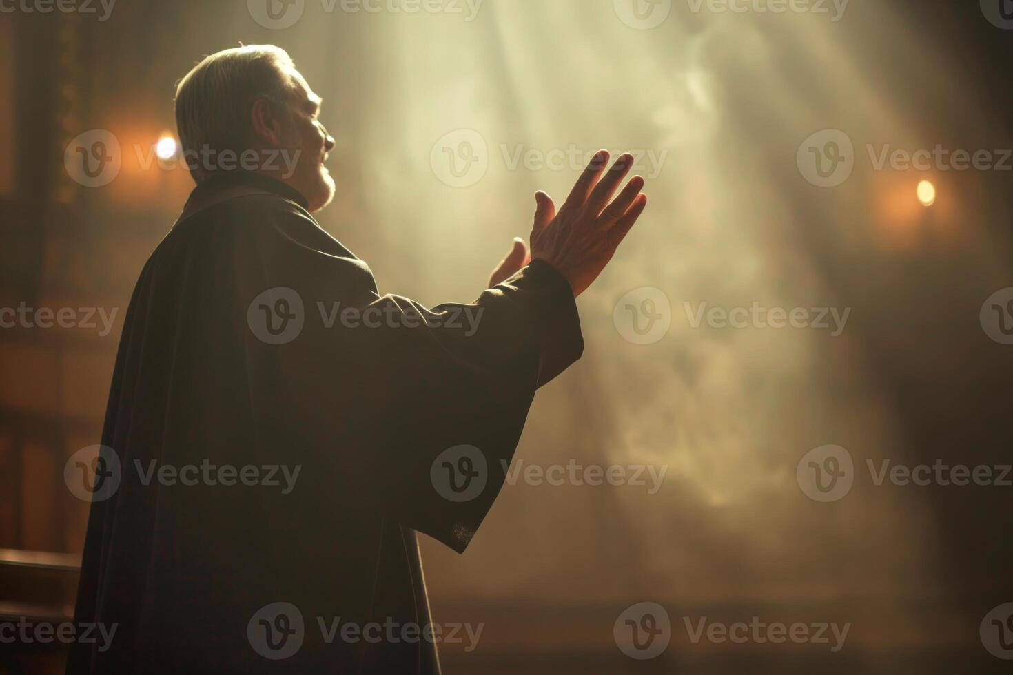 A solemn elderly man in a dark robe raises his hands in a gesture of prayer, illuminated by soft, ethereal light. photo