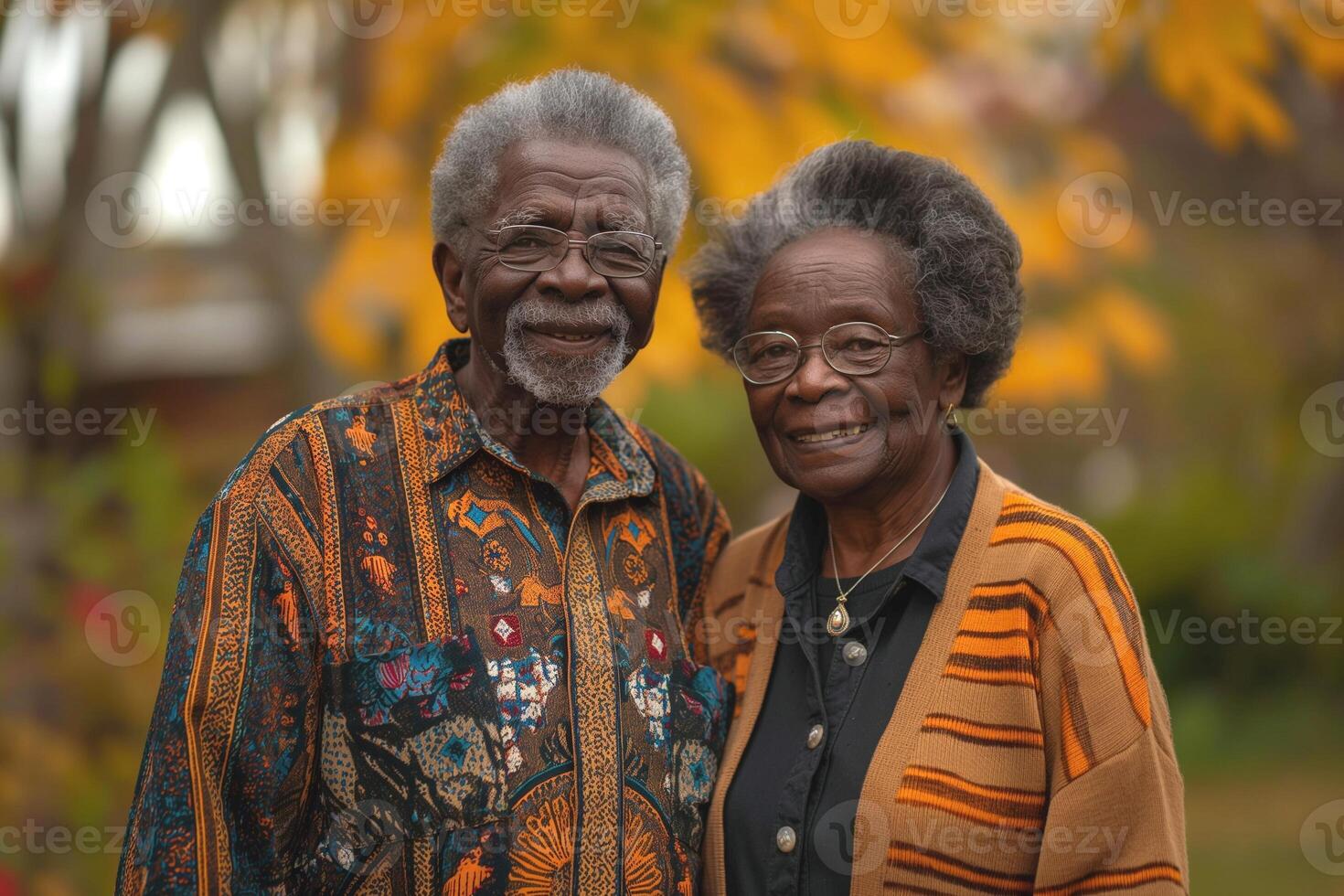 An elderly Black couple smiles warmly, surrounded by autumn leaves, showcasing love and companionship in nature's beauty. photo