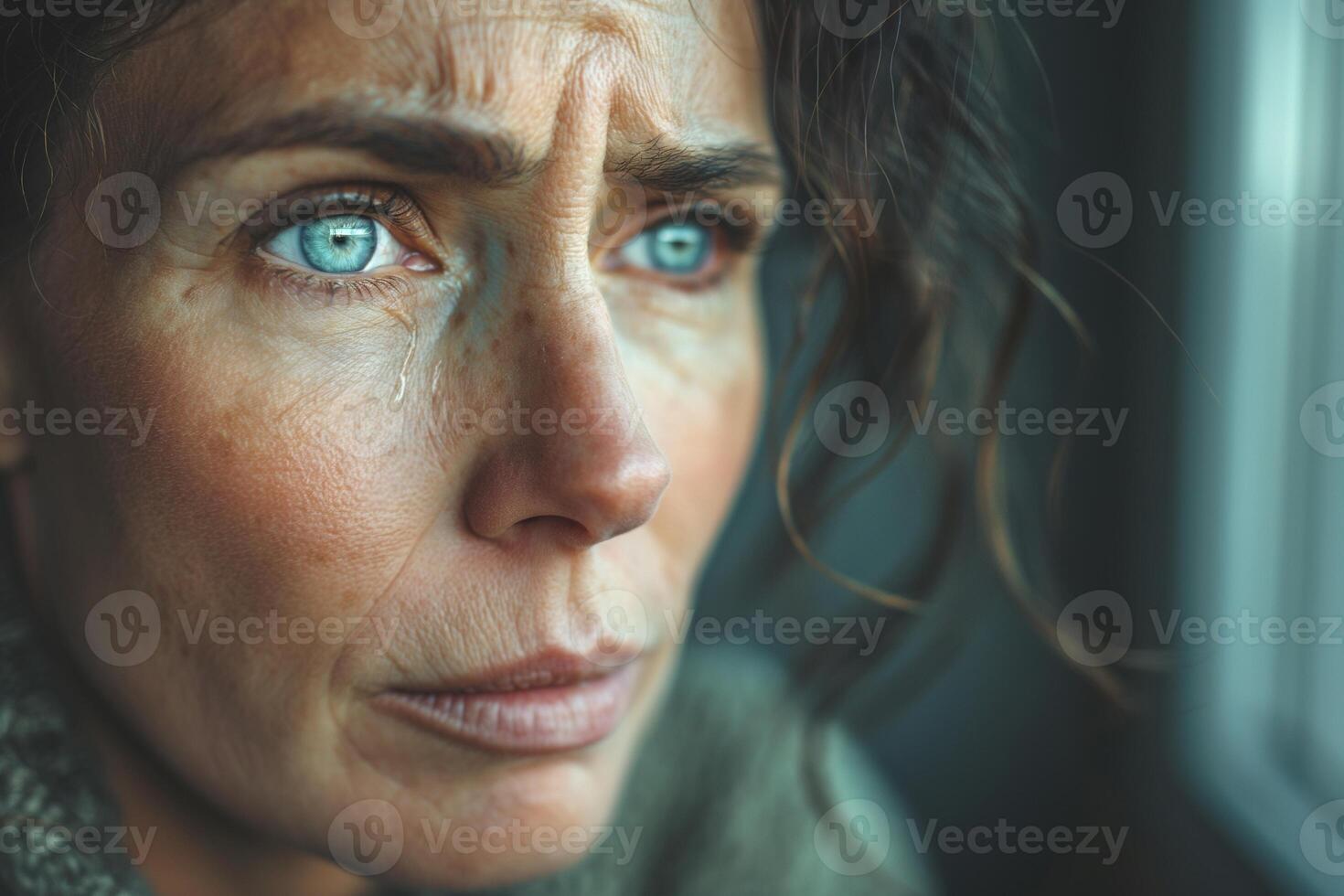 A close-up of a distressed Caucasian woman with striking blue eyes, reflecting deep emotion with a single tear rolling down her cheek. photo
