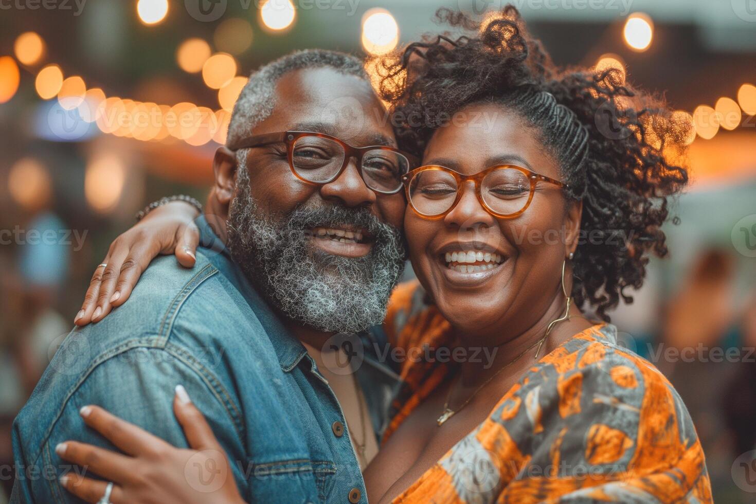 A joyful Black couple smiles together, illuminated by soft, warm lights at a vibrant outdoor gathering. photo