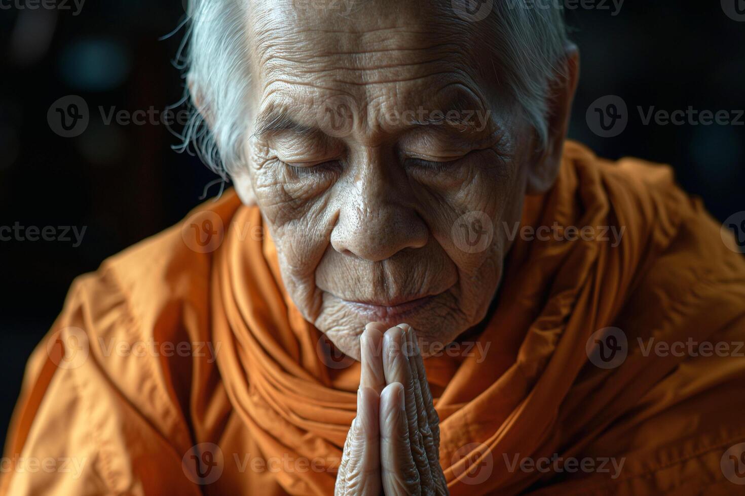 Elderly Asian male monk in orange robes peacefully praying with closed eyes, showcasing serenity and deep spirituality. photo