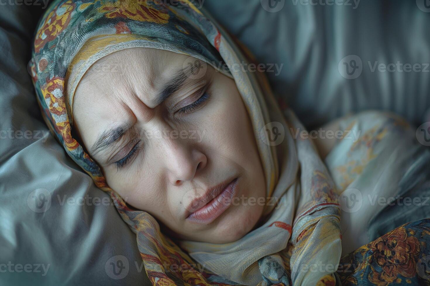 A Middle-Eastern woman with a headscarf resting her head on soft pillows, displaying a contemplative expression. photo
