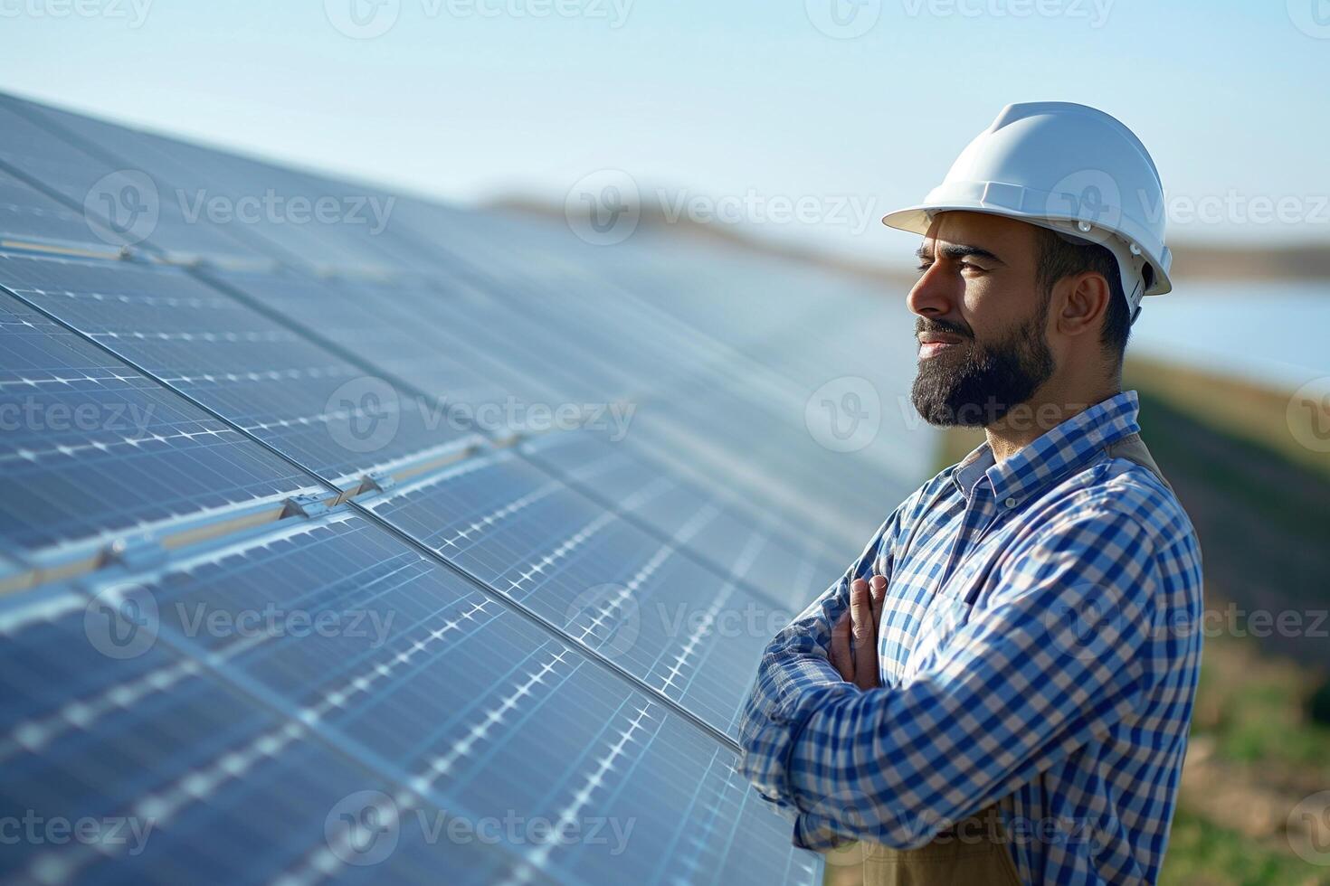 A smiling South Asian man in a hard hat standing proudly in front of solar panels, embodying his dedication to renewable energy. photo
