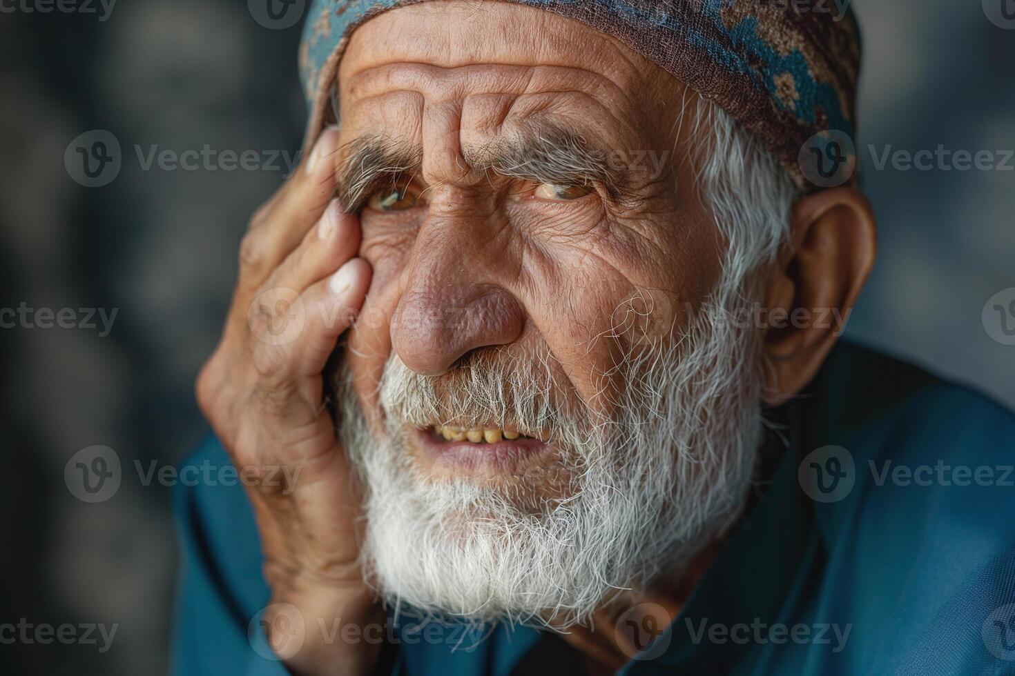 A pensive elderly man with a white beard and distressed expression, wearing a traditional cap against a blurred background. photo