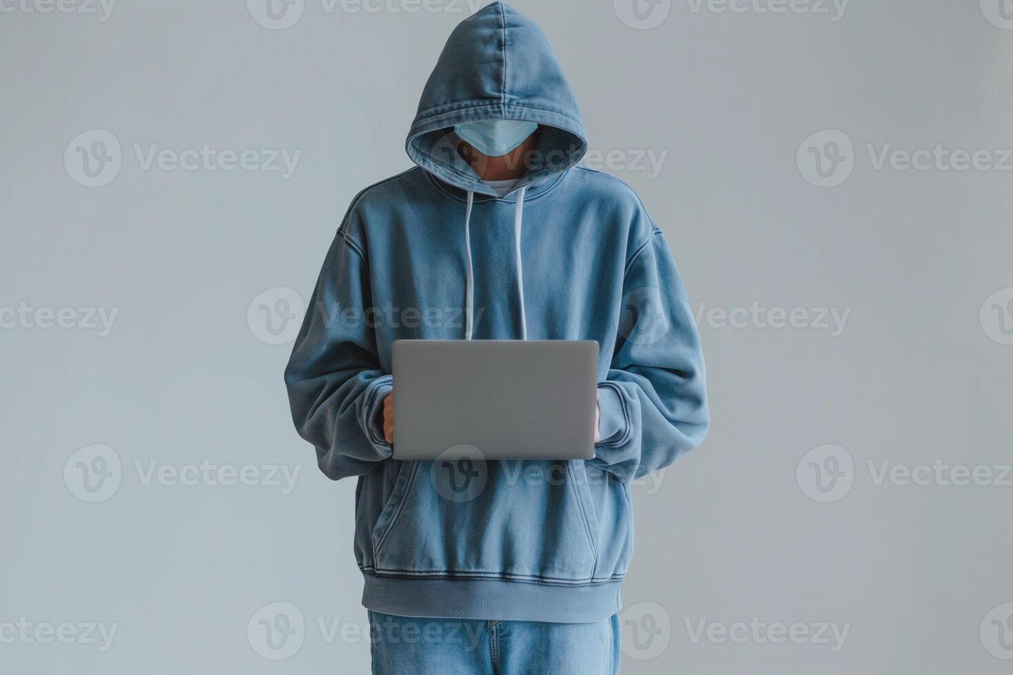 Masked male in a blue hoodie using a laptop, exuding a sense of mystery and modern lifestyle. photo