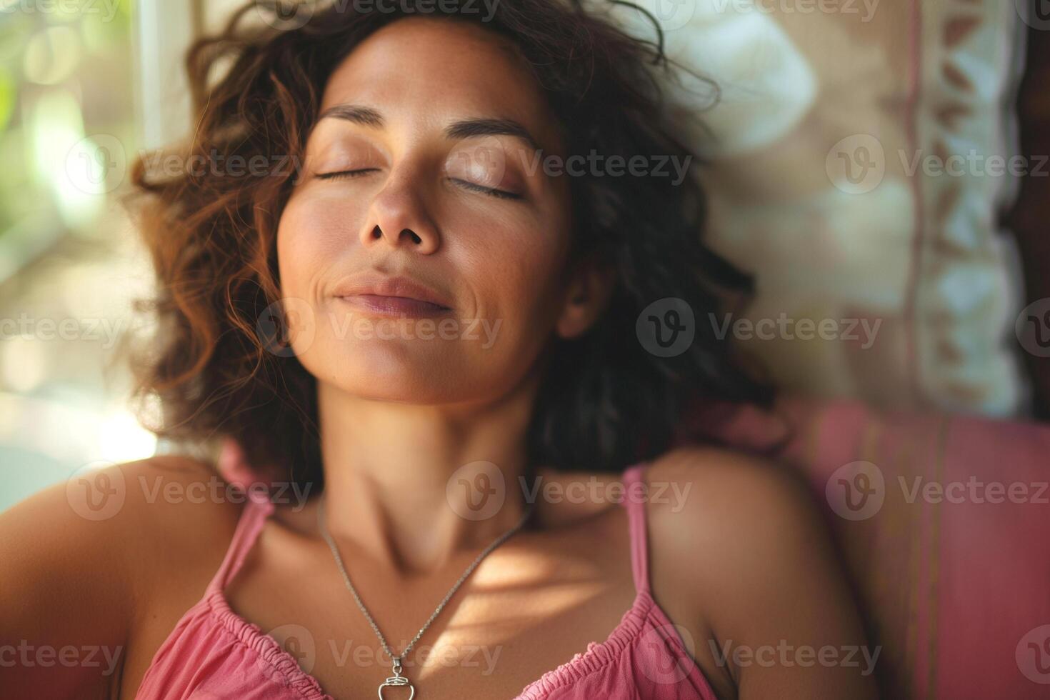 Serene woman with curly hair relaxing indoors, eyes closed, embodying tranquility and peace. photo