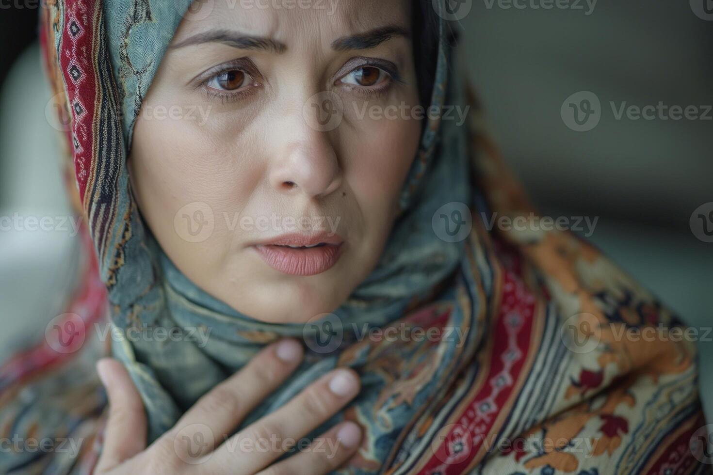 A middle-aged Middle Eastern woman in a colorful scarf looks worried, depicting deep emotion and introspection. photo