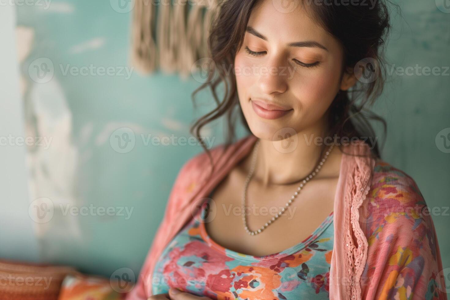 A serene young woman of South Asian descent, gently resting her hand on her belly, exuding calmness in a vibrant, floral outfit. photo