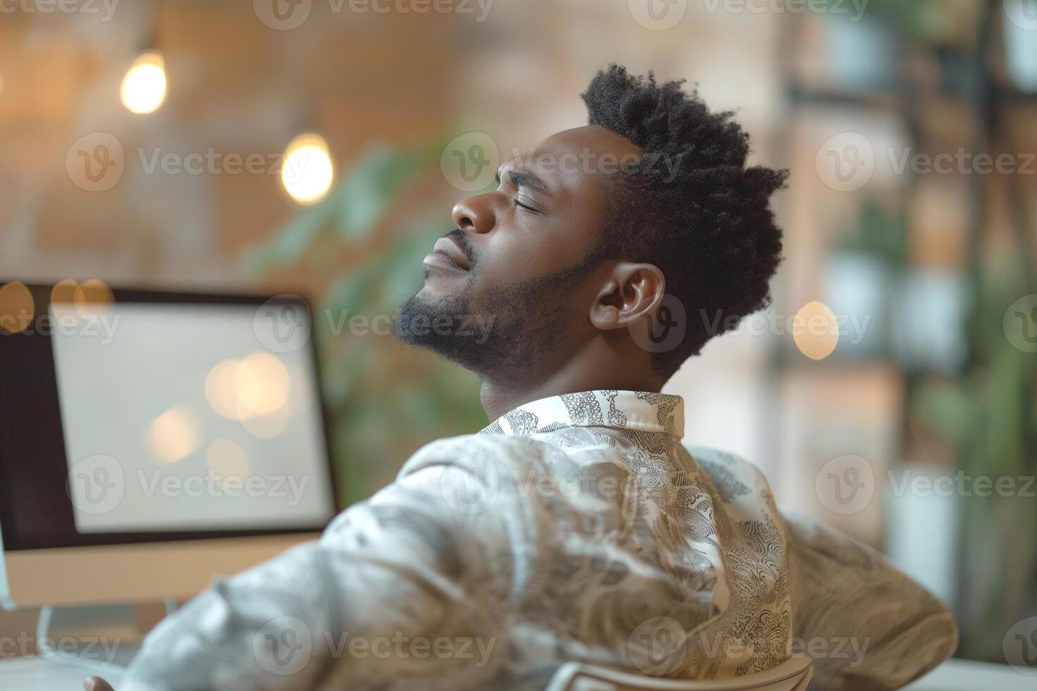 A thoughtful Black man relaxes in a stylish workspace, soaking in the tranquility of his creative environment. photo