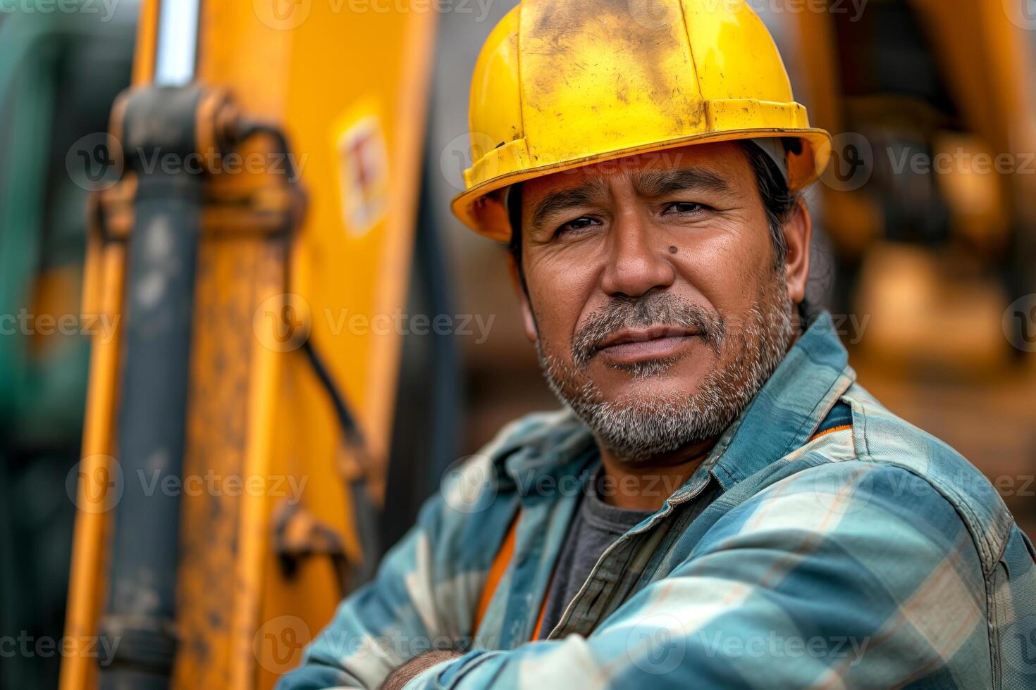 A Hispanic male construction worker in a yellow hard hat, looking confidently at the camera amidst construction machinery. photo