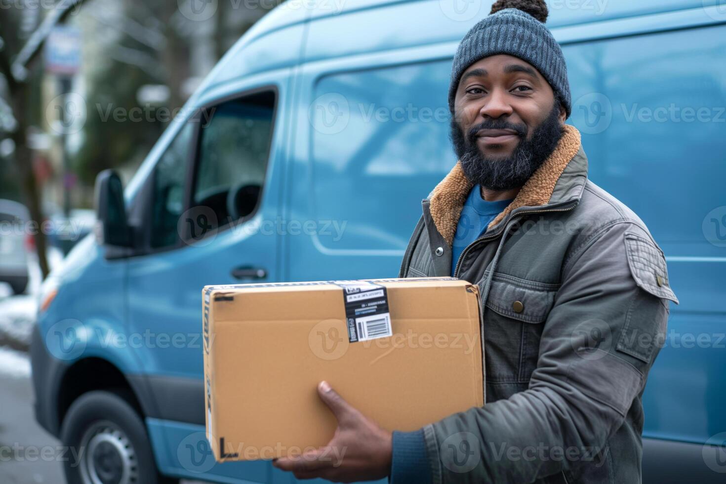 Smiling Black male delivery driver holding a package outside a blue van during winter. photo