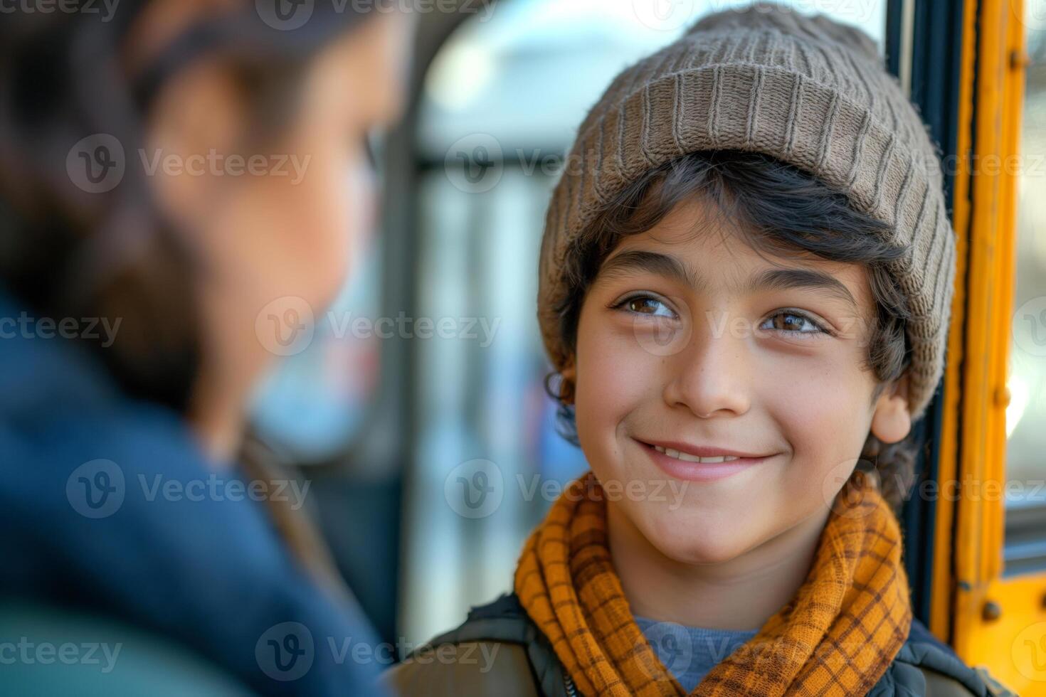 A smiling Middle-Eastern boy wearing a knitted beanie and an orange scarf, joyfully interacting with a woman. photo