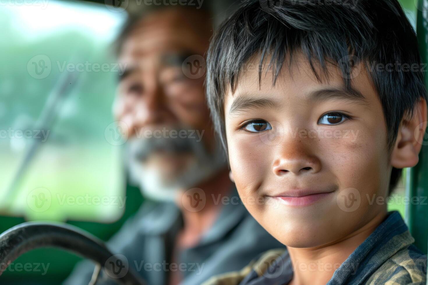 A cheerful Asian boy smiles at the camera while sitting in a vintage vehicle, with an elderly man in the background. photo