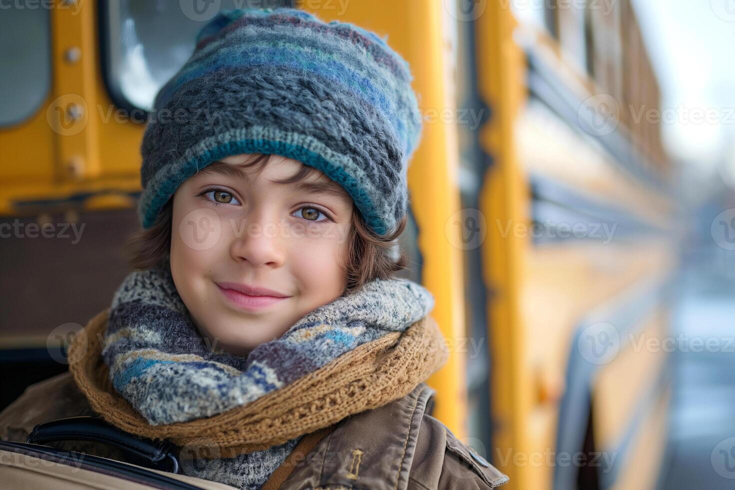 A smiling young boy of Caucasian descent with blue eyes and curly hair, bundled up in winter attire next to a school bus. photo