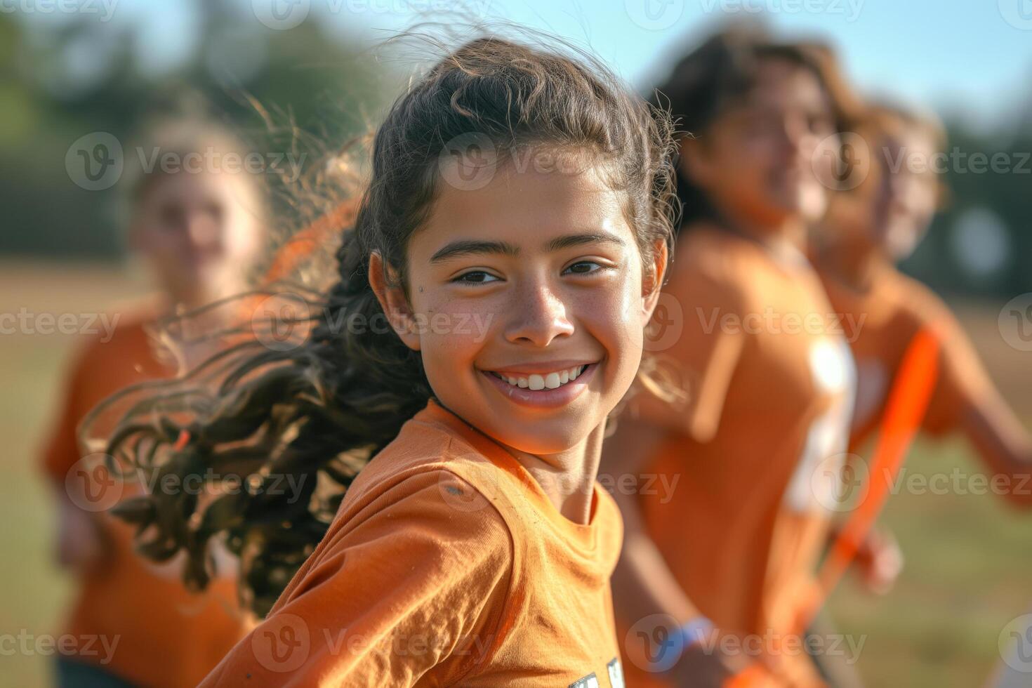 A joyful Hispanic girl, around 10 years old, smiles brightly while running with friends in an outdoor sports setting. photo