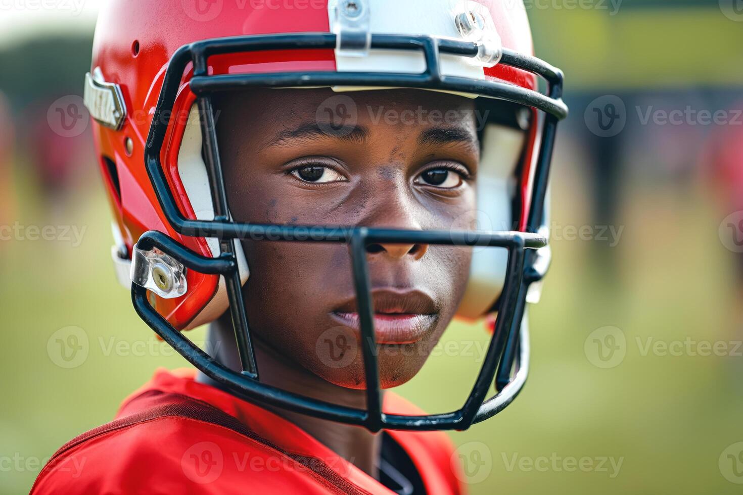 A young African American boy in a football helmet poses thoughtfully, showcasing determination and focus at practice. photo